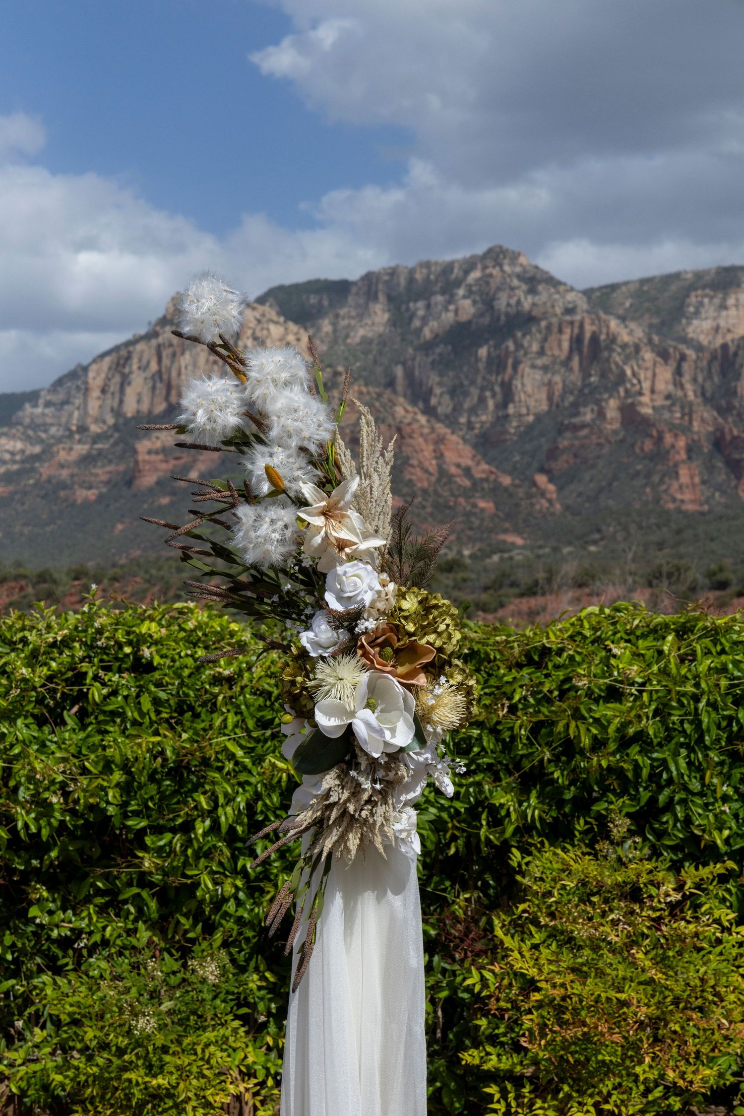 Floral wedding arch with white flowers and dried botanicals set against red rock mountains in Sedona, Arizona.