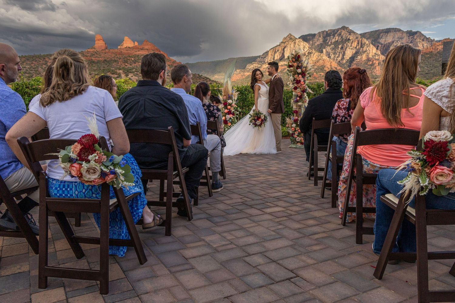 Rows of guests seated in outdoor chairs at a sunset wedding ceremony with dramatic mountain backdrop.