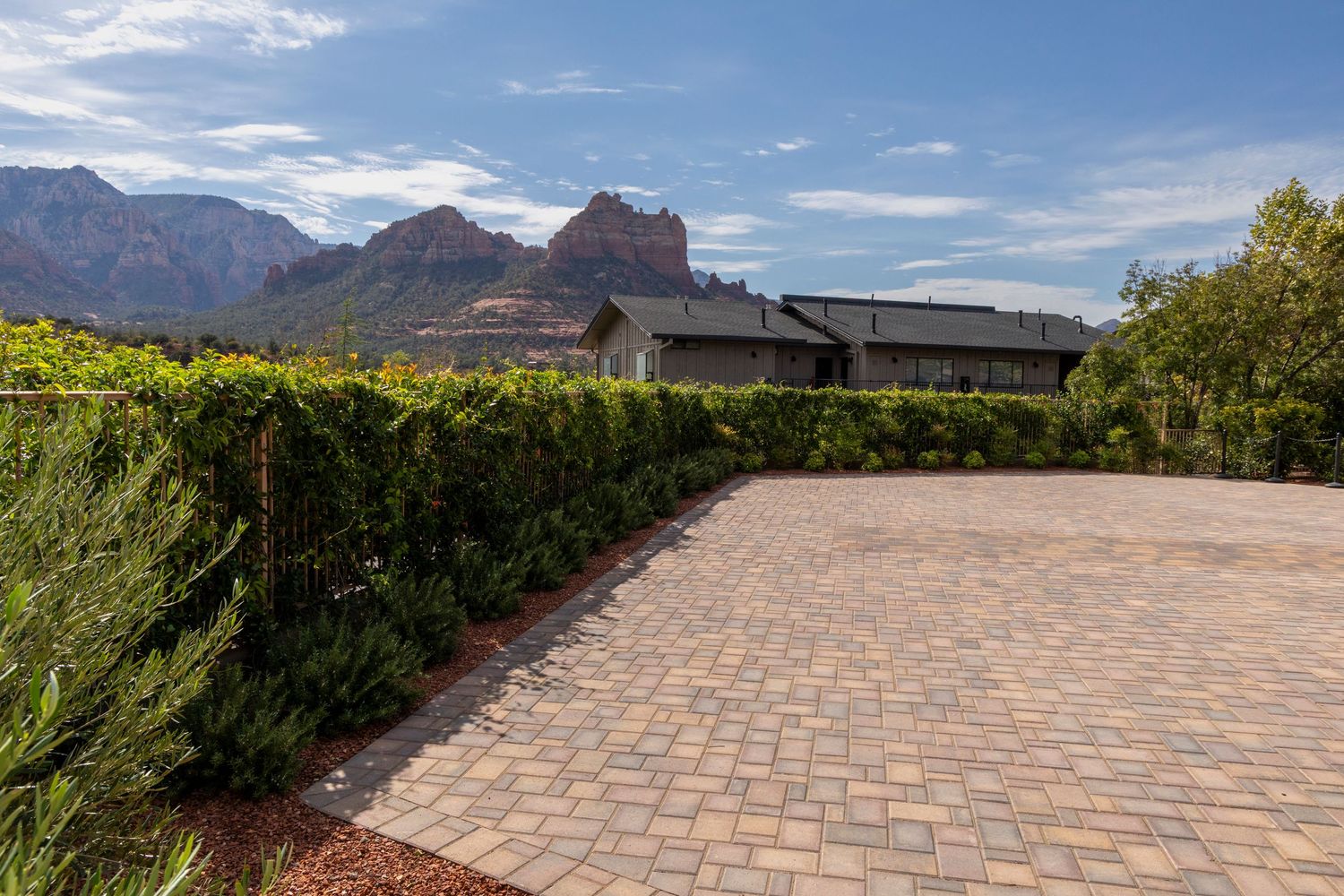 A curved brick paver pathway leads through a garden with mountains visible in the background under blue skies.