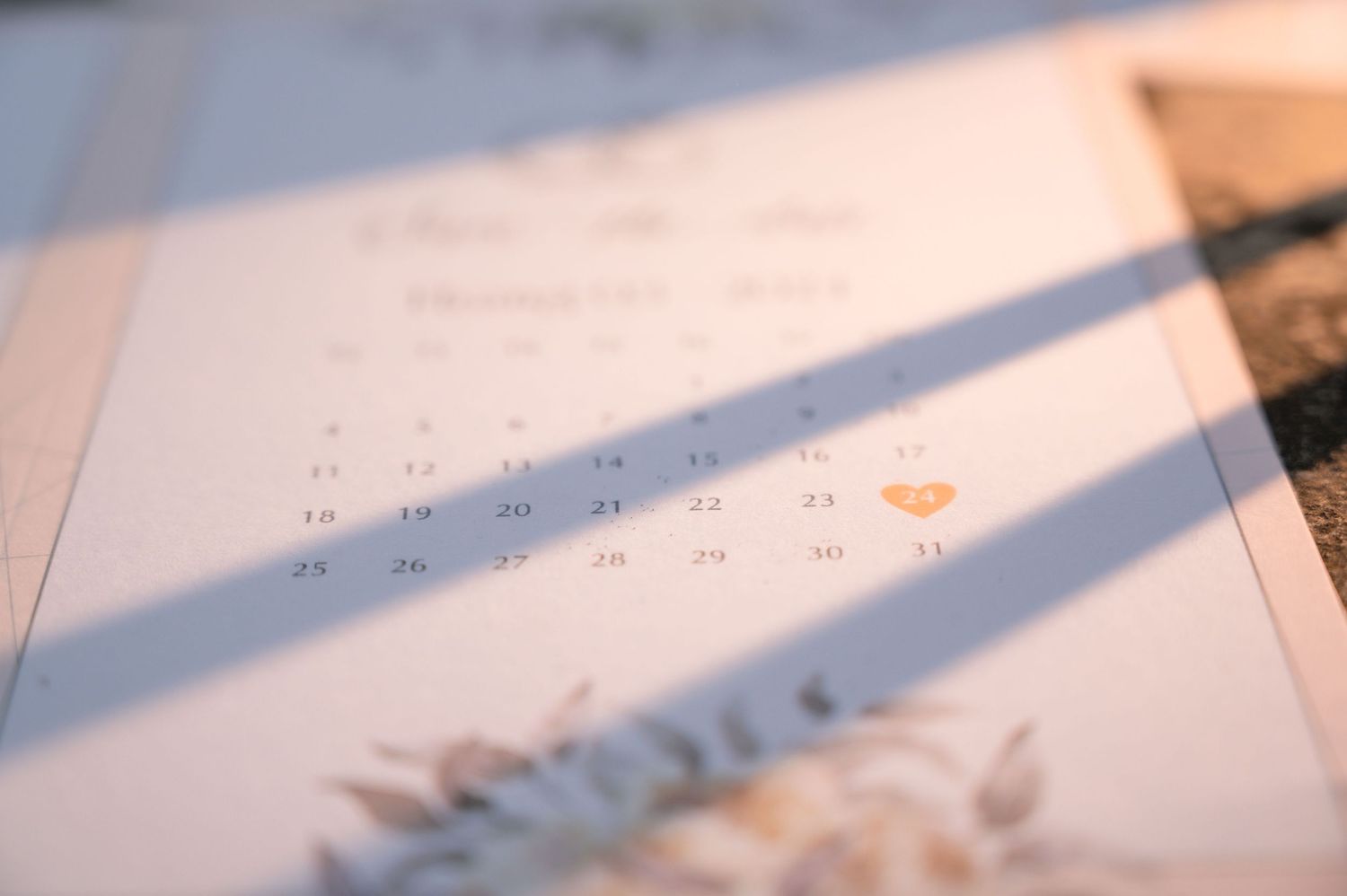 Close-up of a wedding save-the-date calendar with a heart marking a special date in warm sunlight.