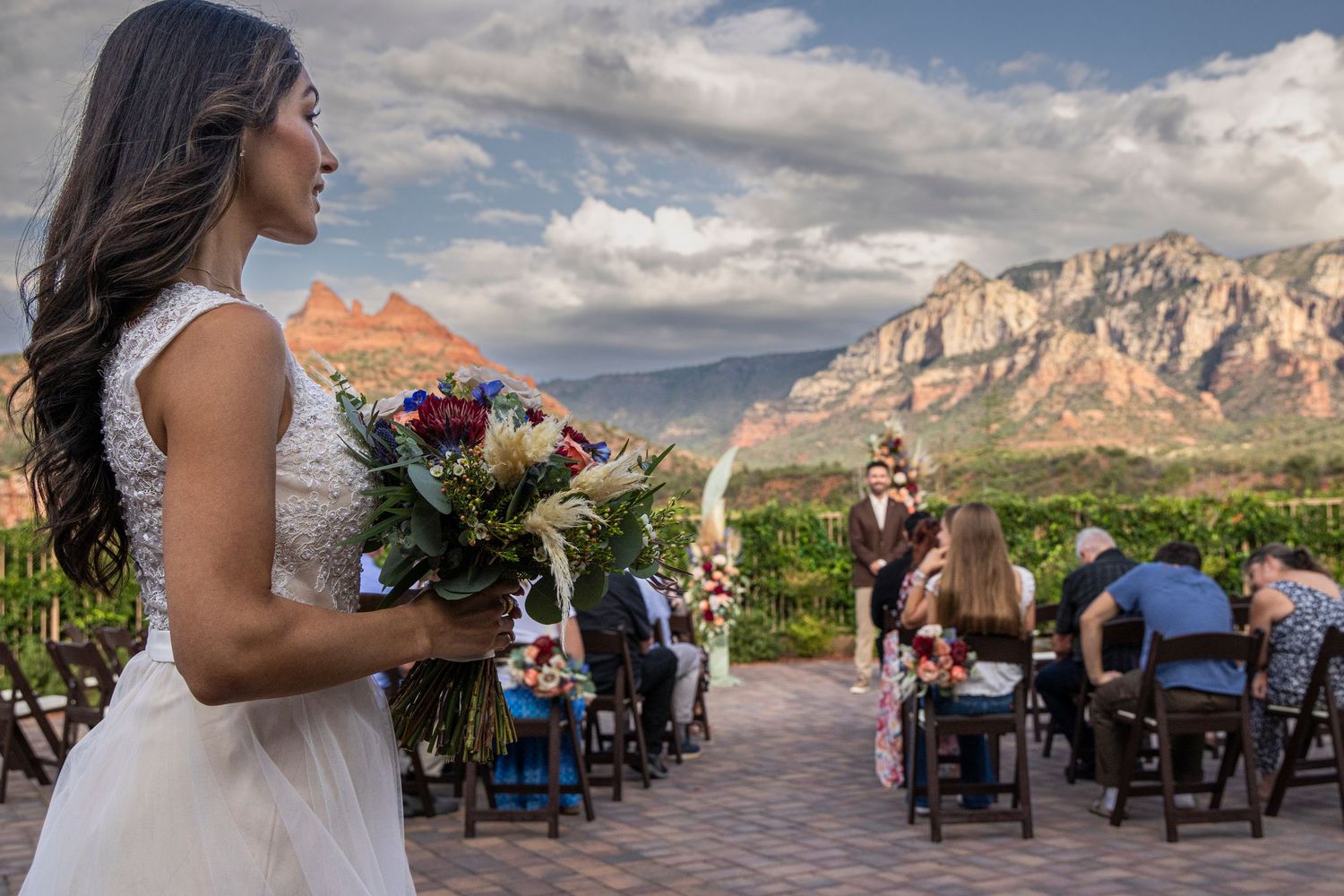 Bride in white gown holds bouquet at outdoor Sedona wedding with red rock mountains backdrop.