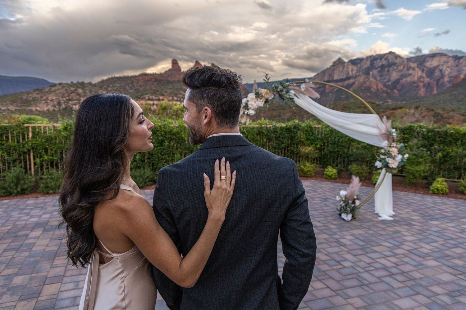 A couple shares a romantic moment on a paved terrace overlooking majestic red rock mountains at sunset.