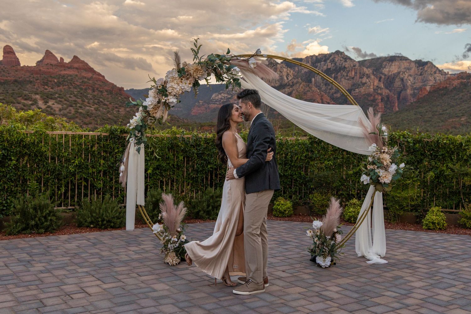 A couple shares a romantic moment during their sunset wedding ceremony against a backdrop of dramatic mountain peaks.