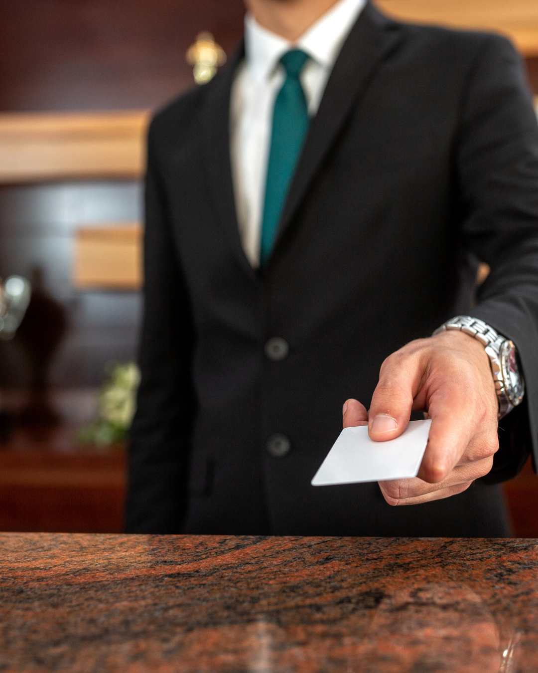 Professional in suit holding business card over marble counter surface.