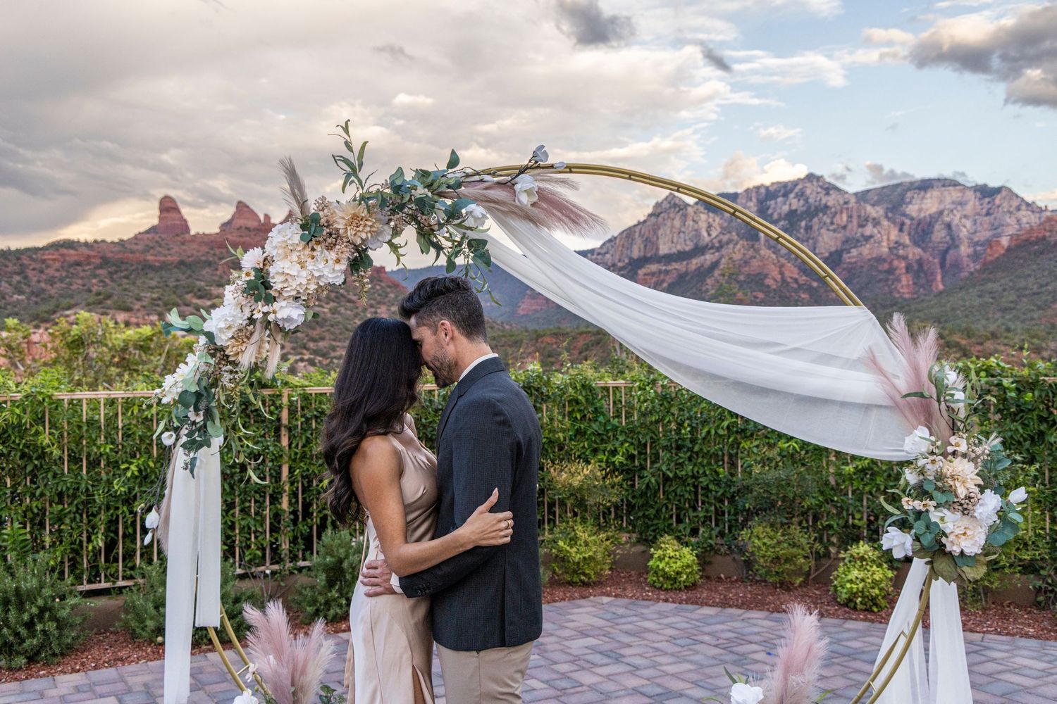 A romantic outdoor wedding ceremony in Sedona with red rock mountains and white flowing fabric arch decorations.