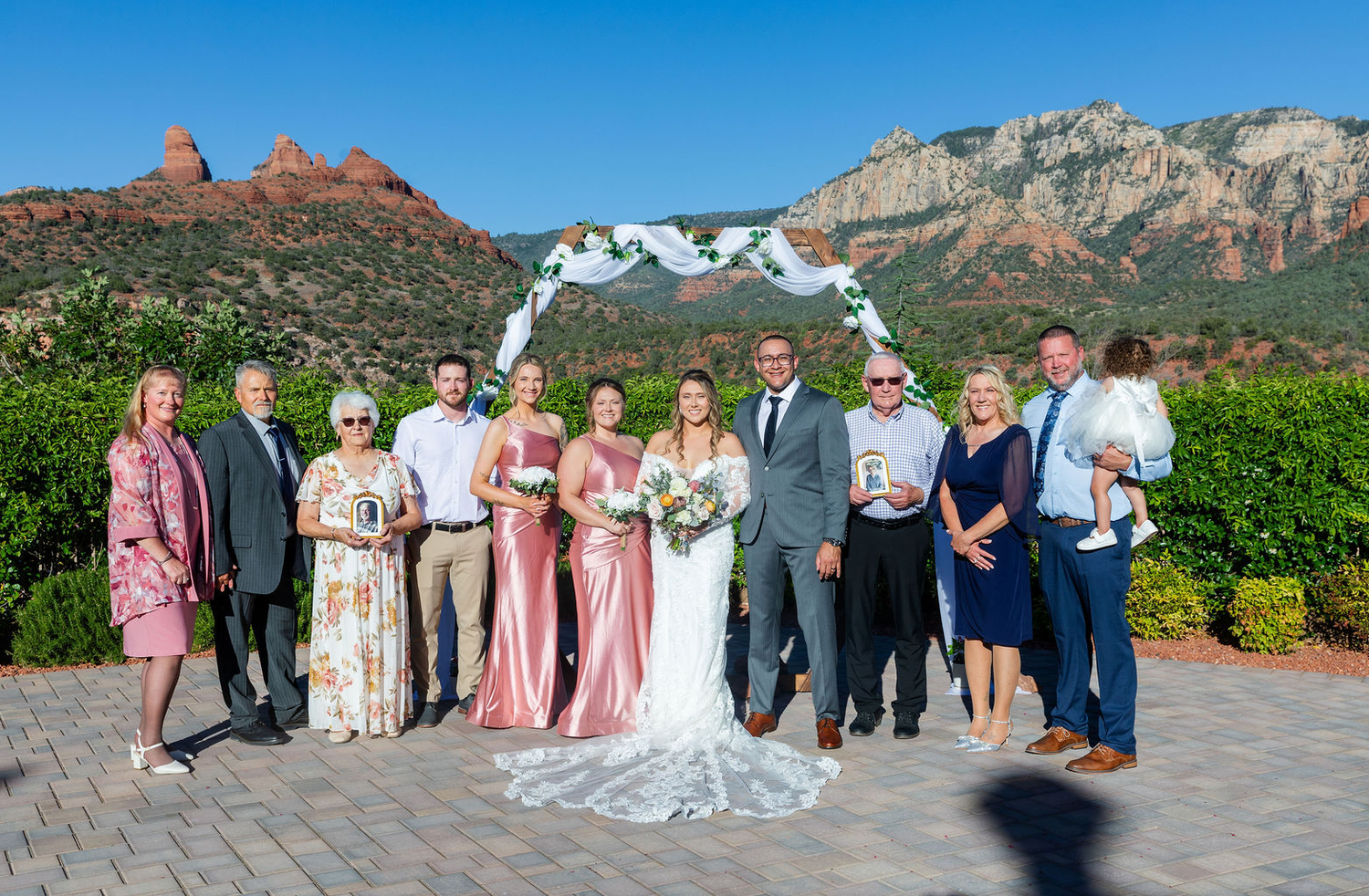Wedding party poses before red rock formations in Sedona, Arizona, with floral arch backdrop.