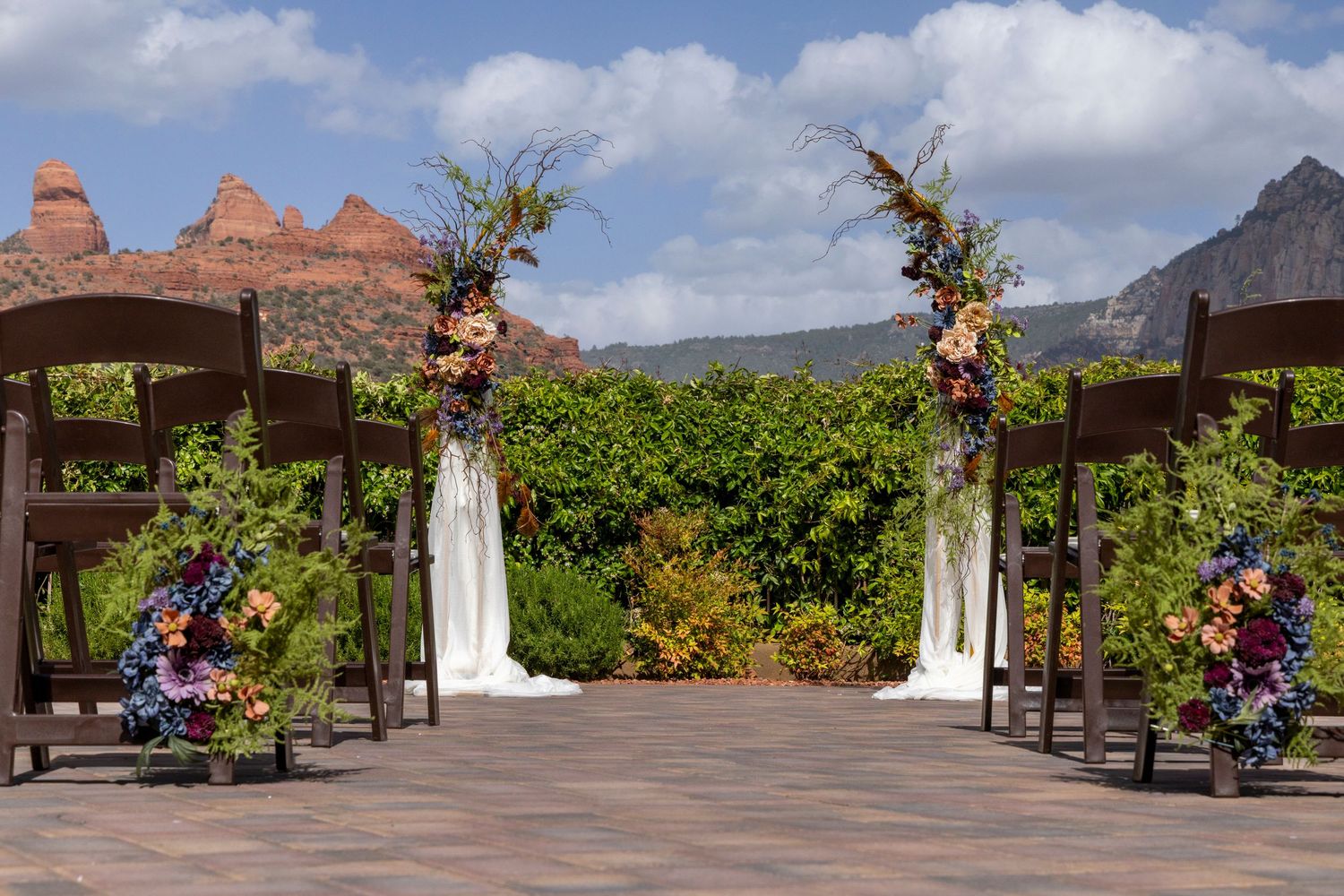 Outdoor wedding ceremony setup with floral arch, dark wood chairs, and stunning red rock Sedona landscape backdrop.