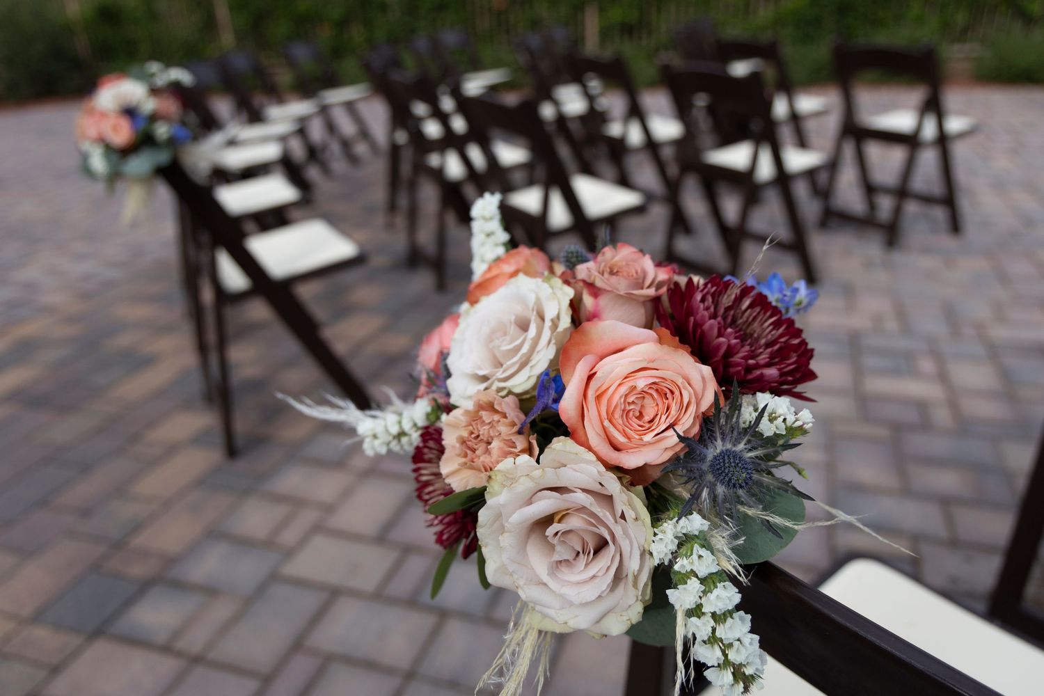 Wedding ceremony seating is adorned with elegant pink and burgundy rose bouquets on a paved patio setting.