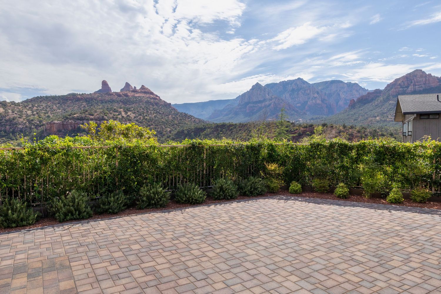 Brick paver patio with lush green hedges and stunning red rock mountain views under a partly cloudy sky in Sedona, AZ.