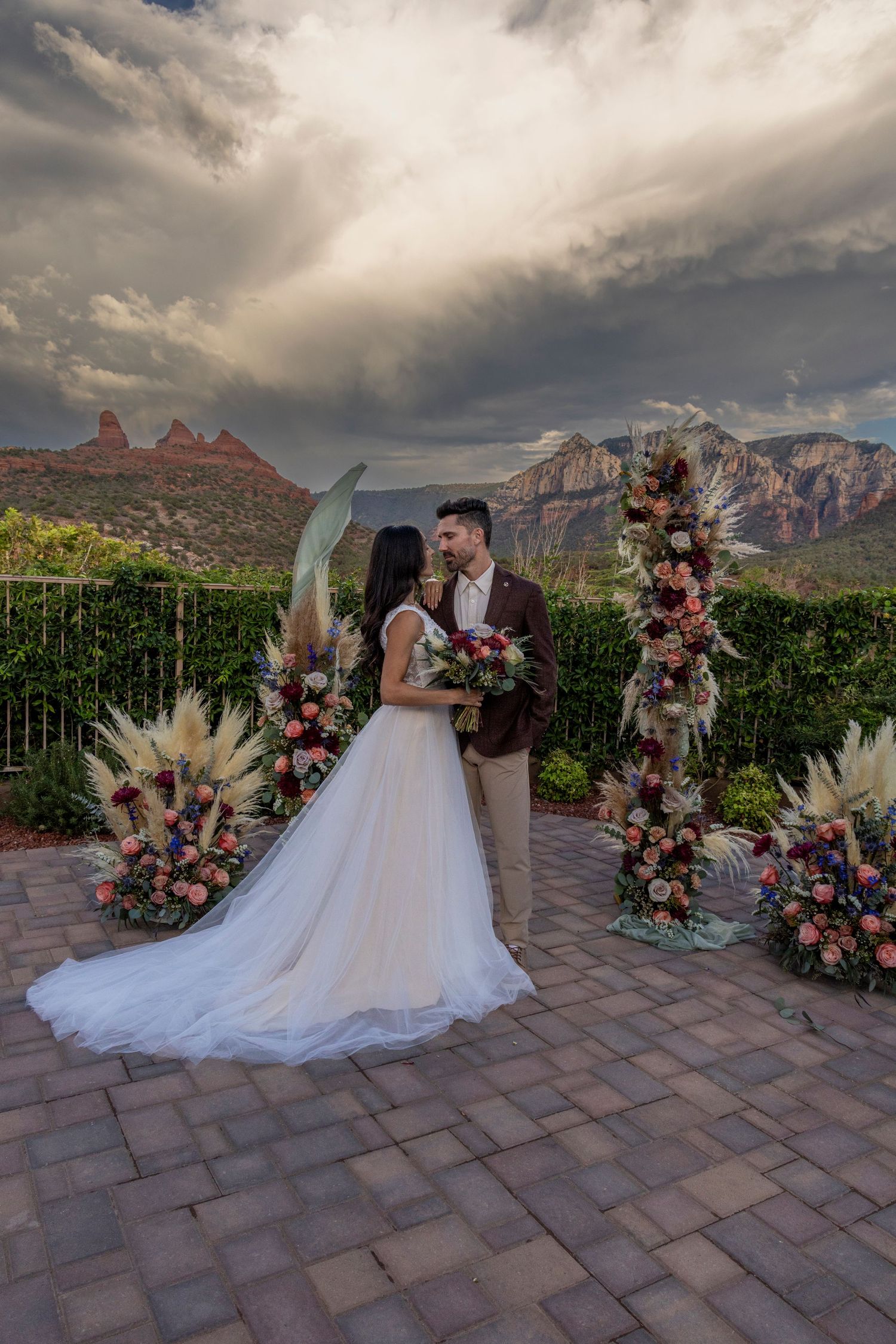 A romantic wedding ceremony takes place on a scenic terrace overlooking majestic red rock formations in Sedona at sunset.