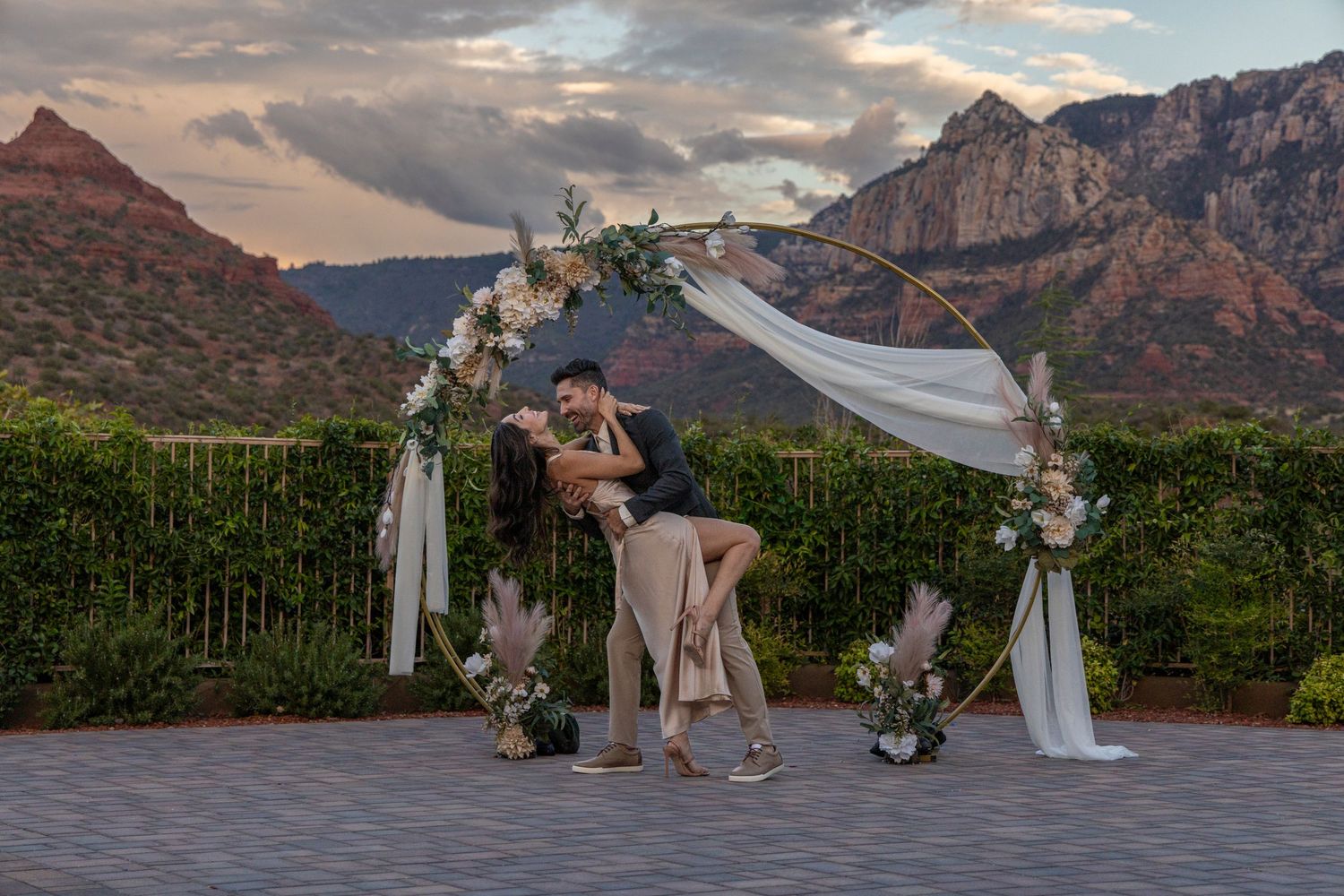 Outdoor wedding ceremony setup with dramatic mountain backdrop and cloudy skies at sunset.