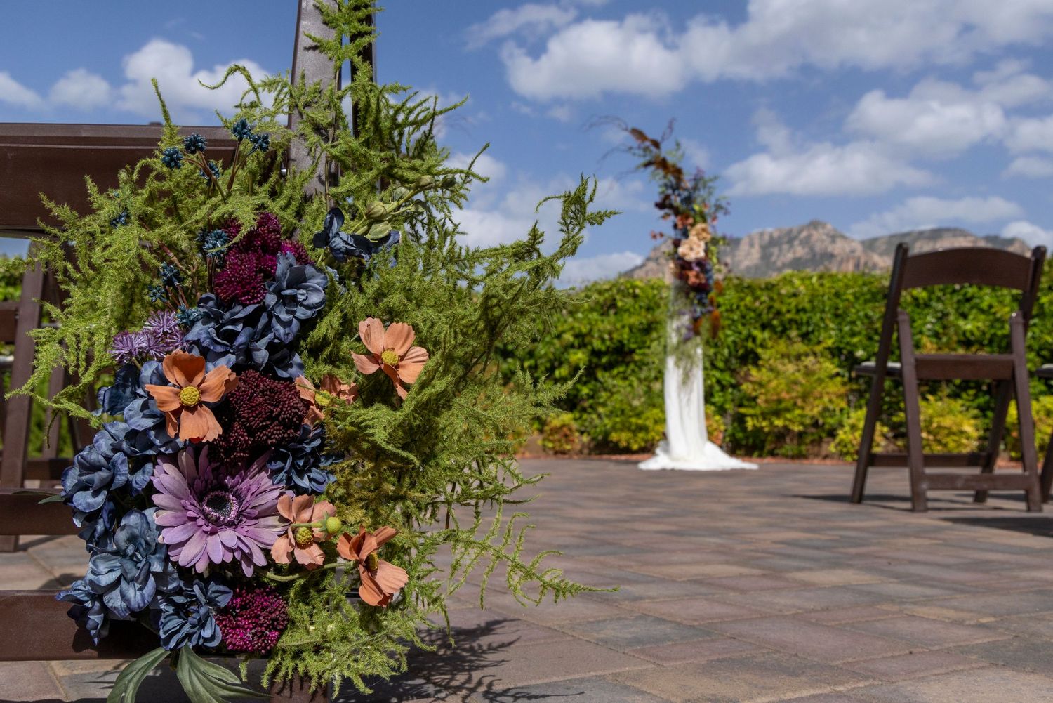 Colorful wedding ceremony floral arrangements with blue, purple, and orange blooms on a patio with mountain views.