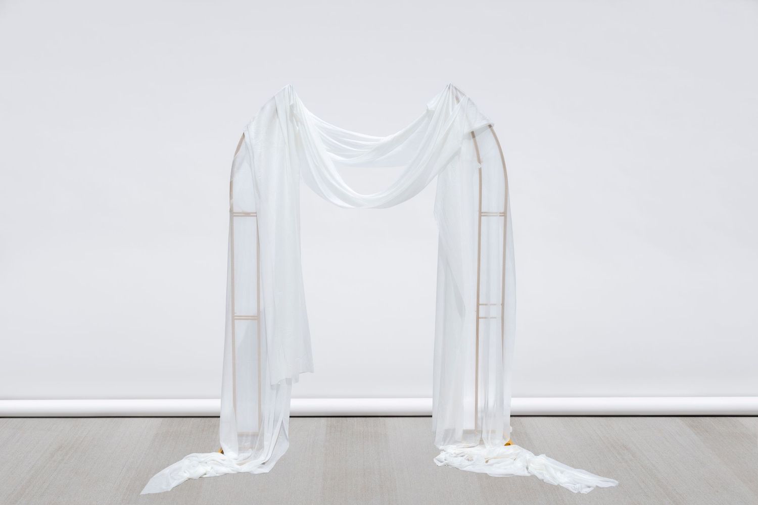 Modern gold frame arch with draped white fabric creates elegant ceremony backdrop.