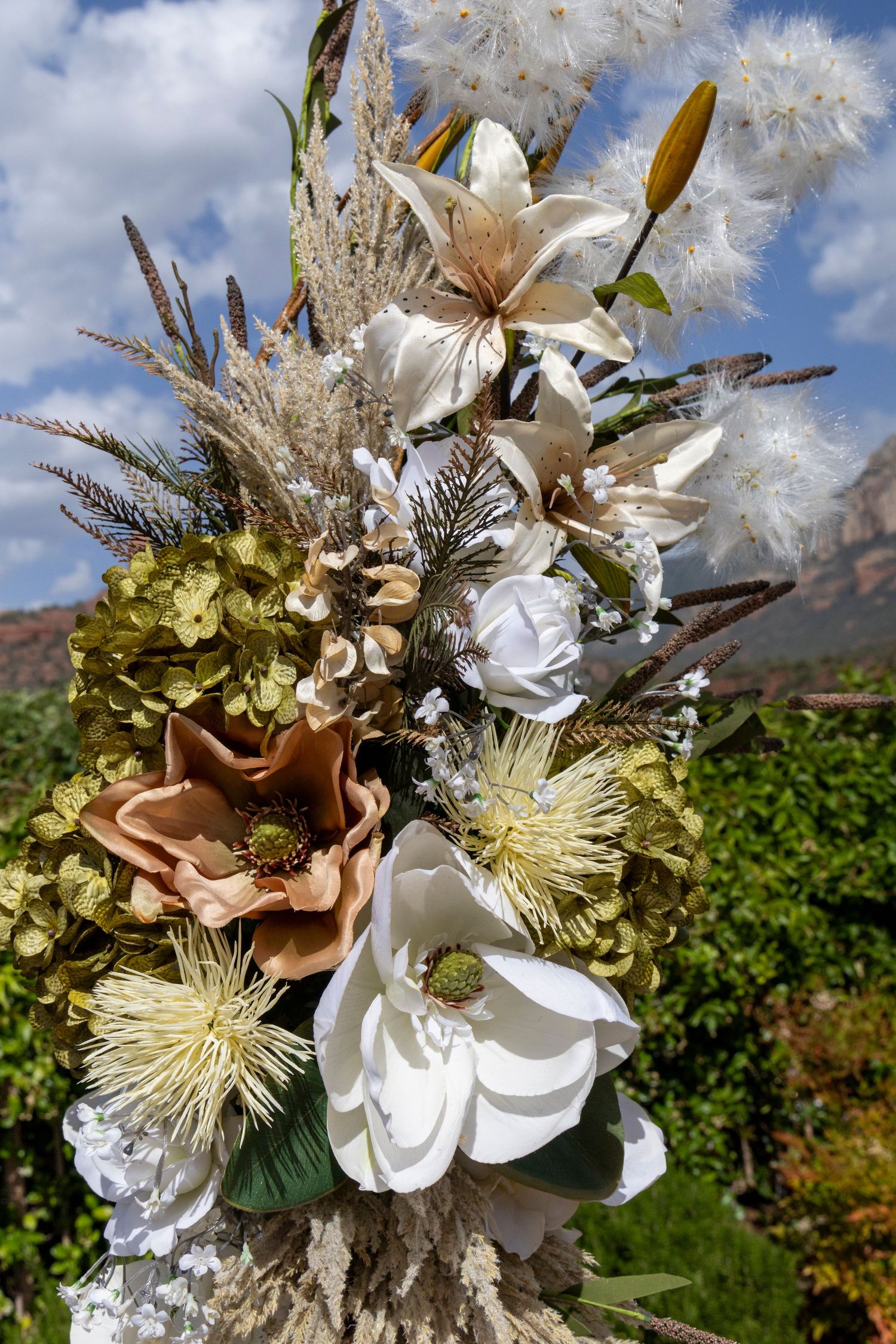 Elegant wedding bouquet with white lilies, magnolias, dried pampas grass, and greenery against a blue sky backdrop.
