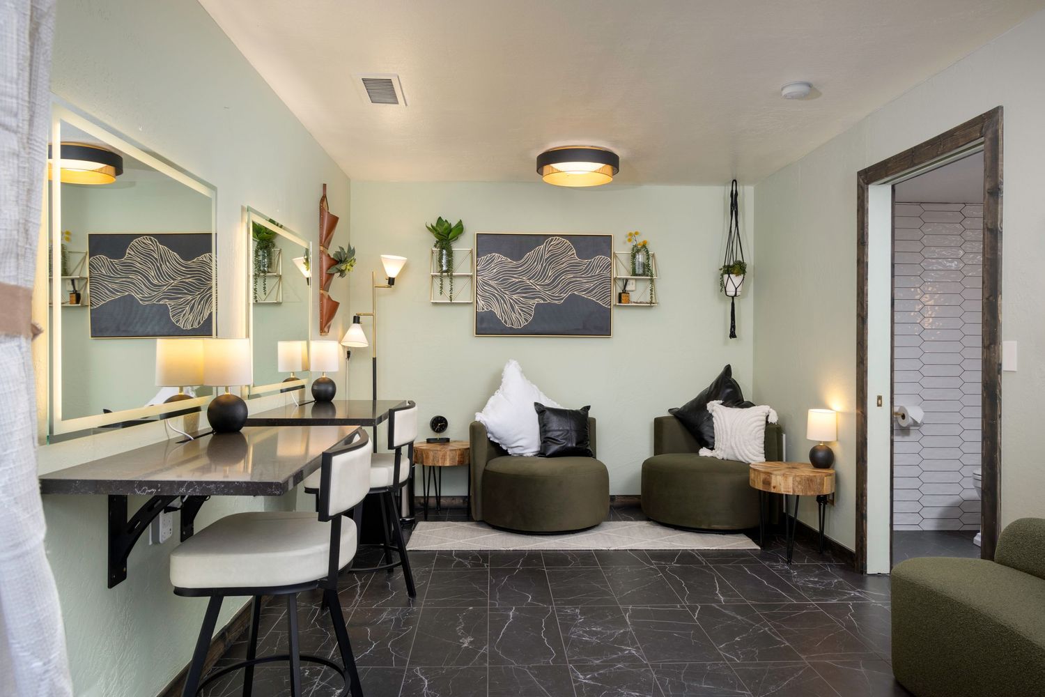 Modern hotel room with green accent walls, marble floors, lounge chairs, and a built-in desk with mirror.