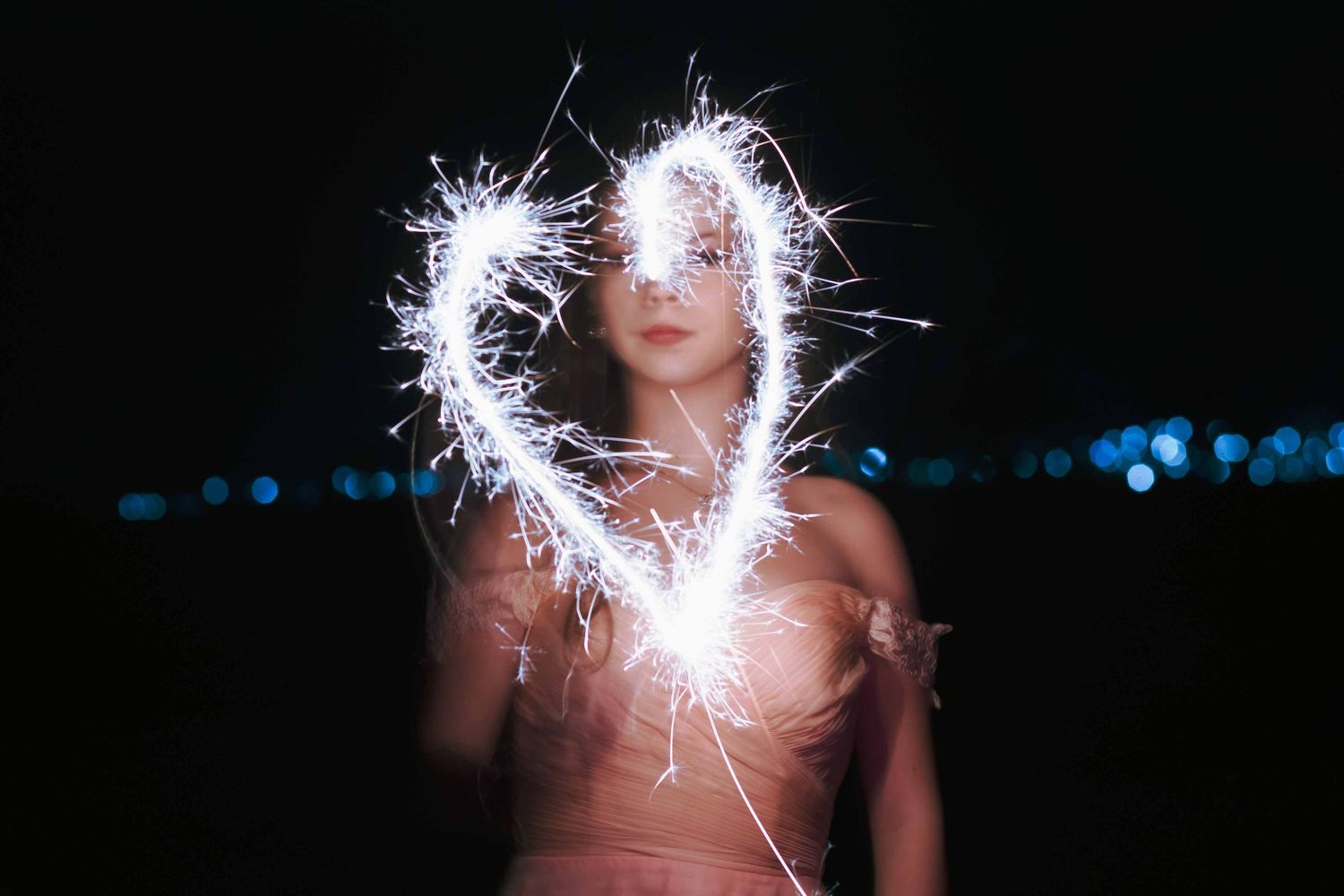 Creative night portrait surrounded by sparklers creating a heart-shaped light effect.