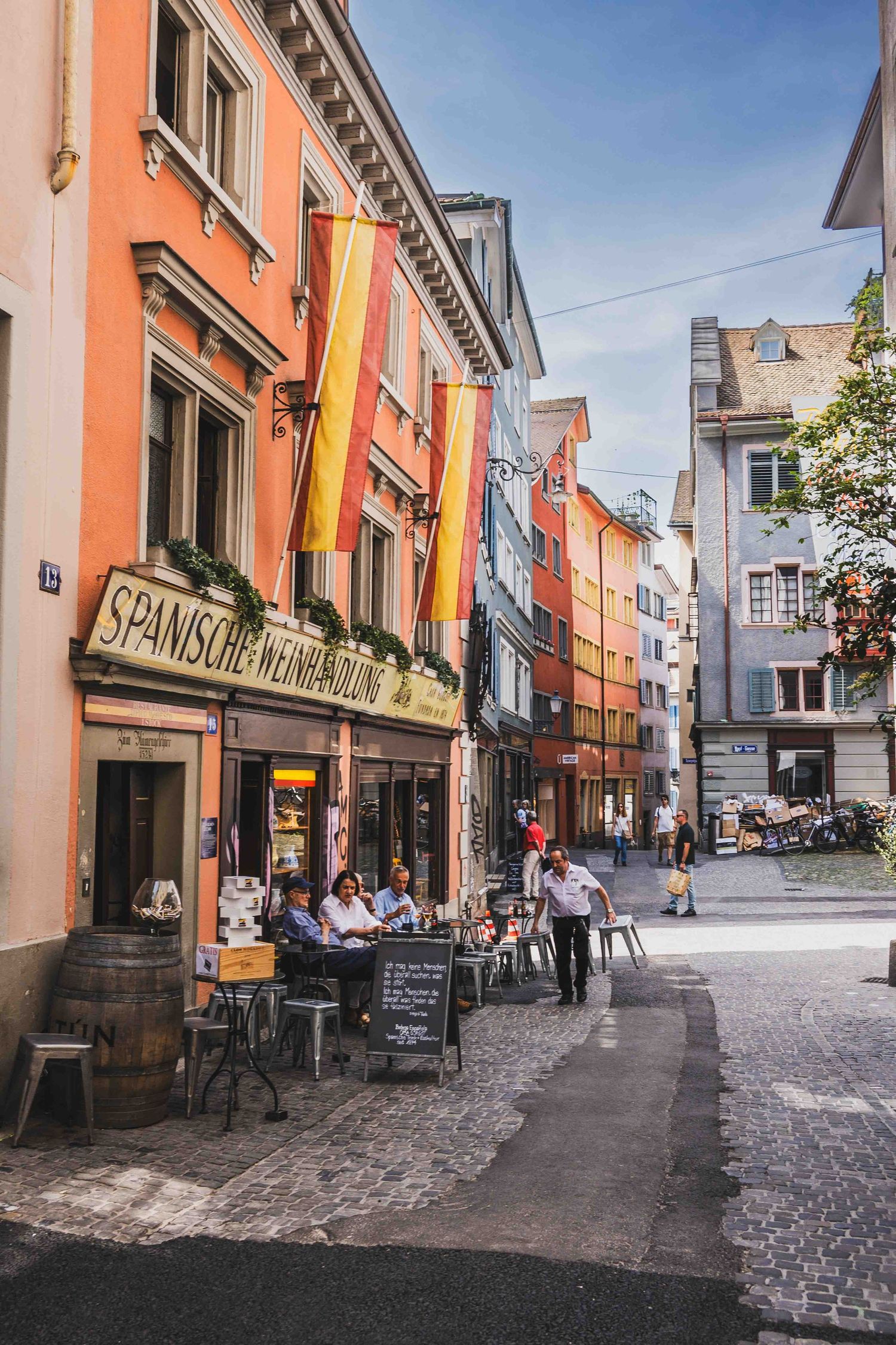 Colorful historic street in Germany with outdoor cafe seating and hanging flags on orange and yellow buildings.