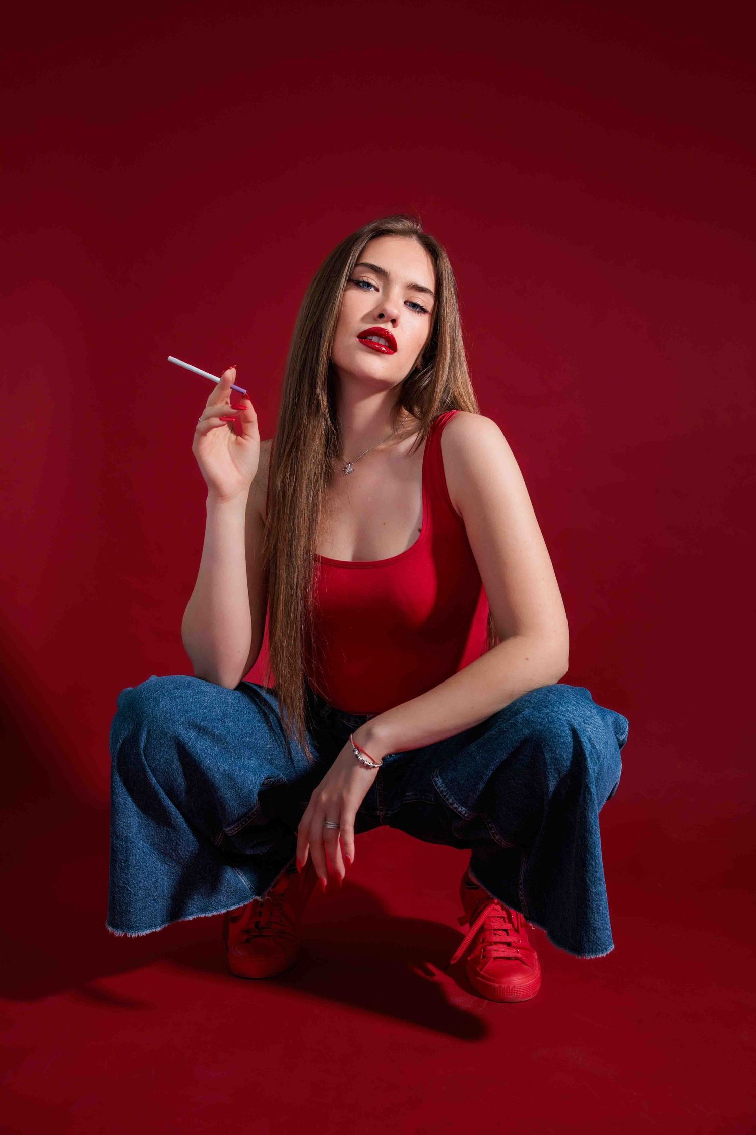 A figure in red poses expressively against a deep burgundy background wearing jeans in an artistic photo series.
