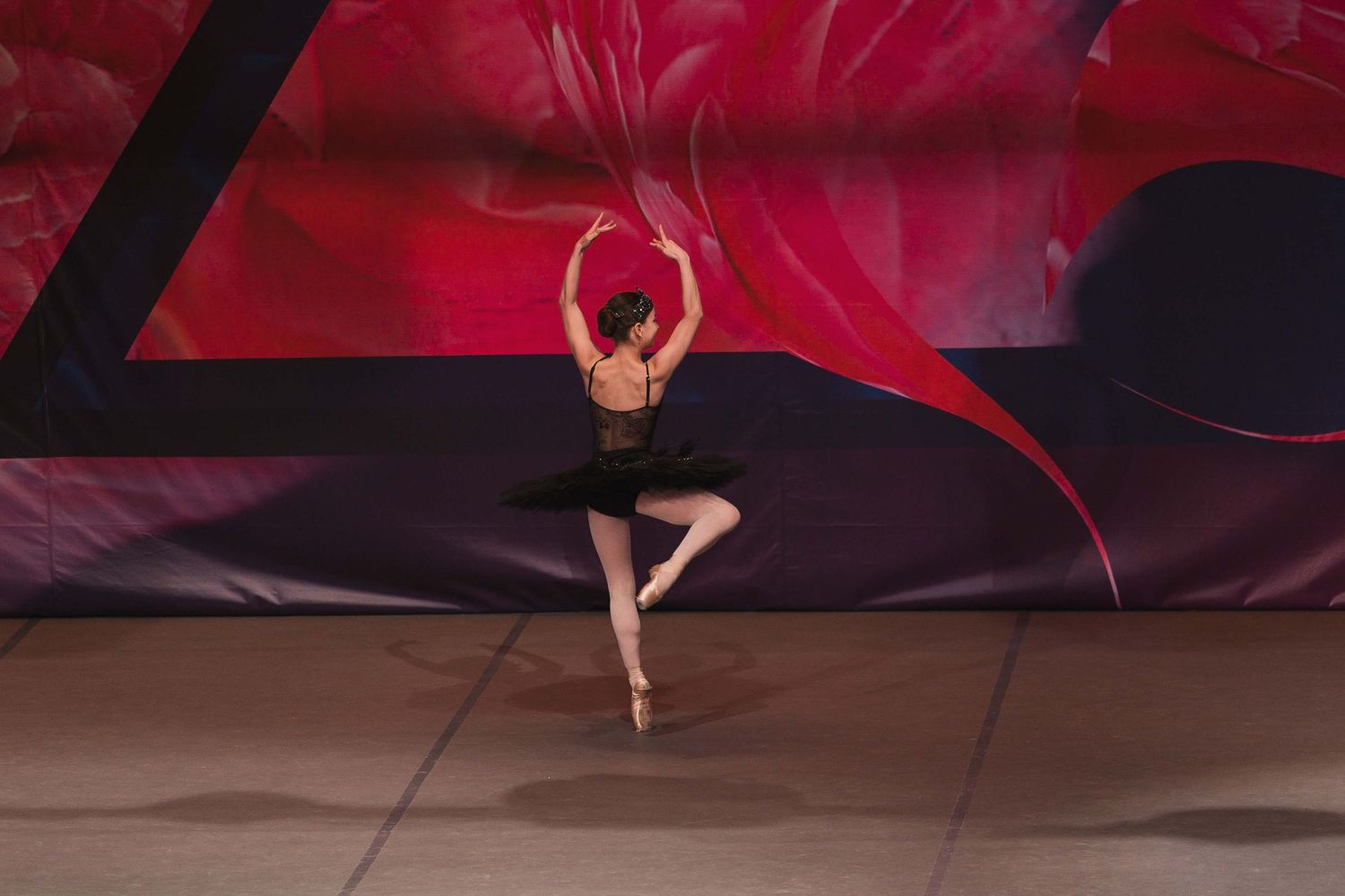 A ballet dancer performs a graceful pose on pointe against a dramatic red and black backdrop.