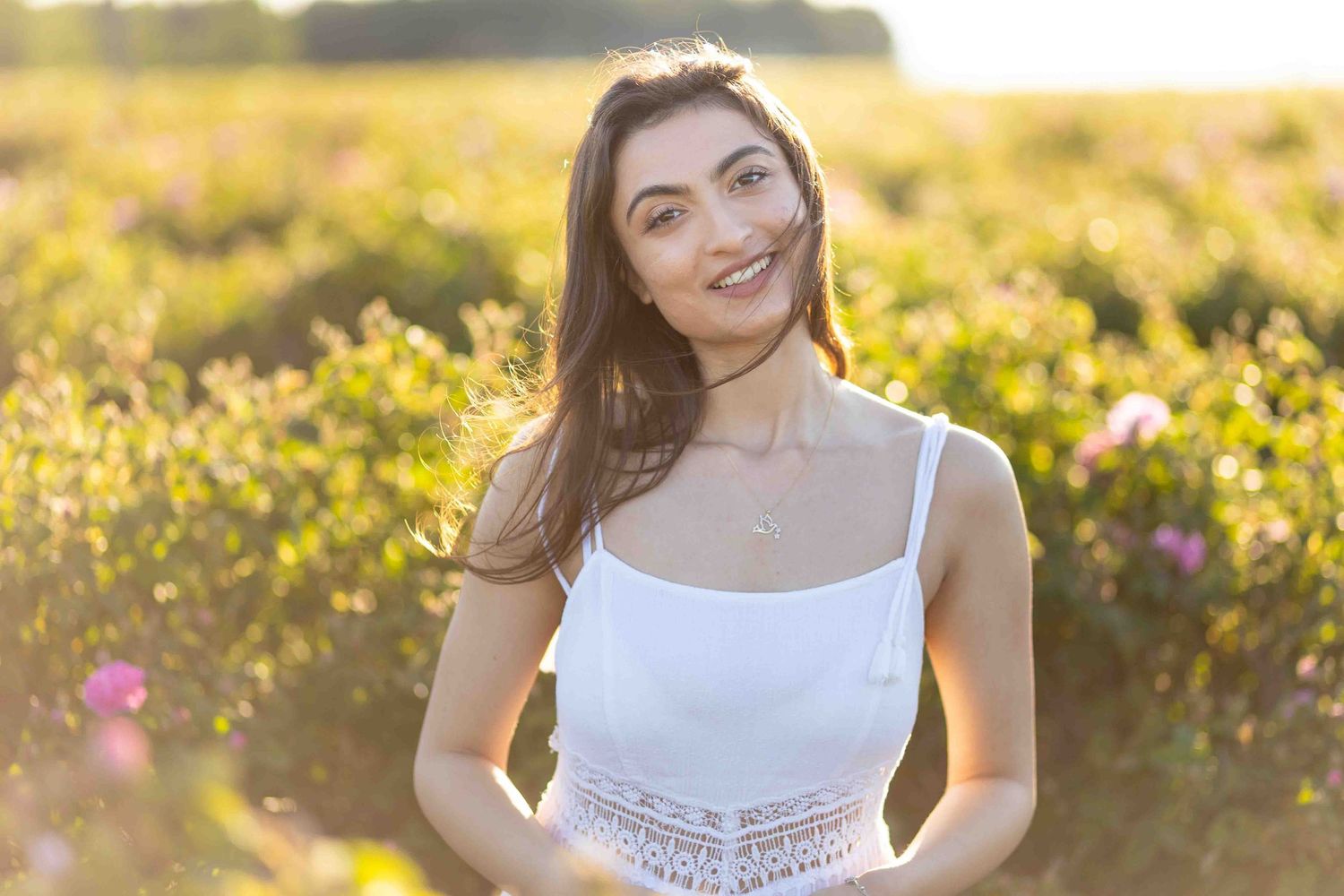 Person in flowing white dress laughing in a golden sunlit flower garden during sunset.