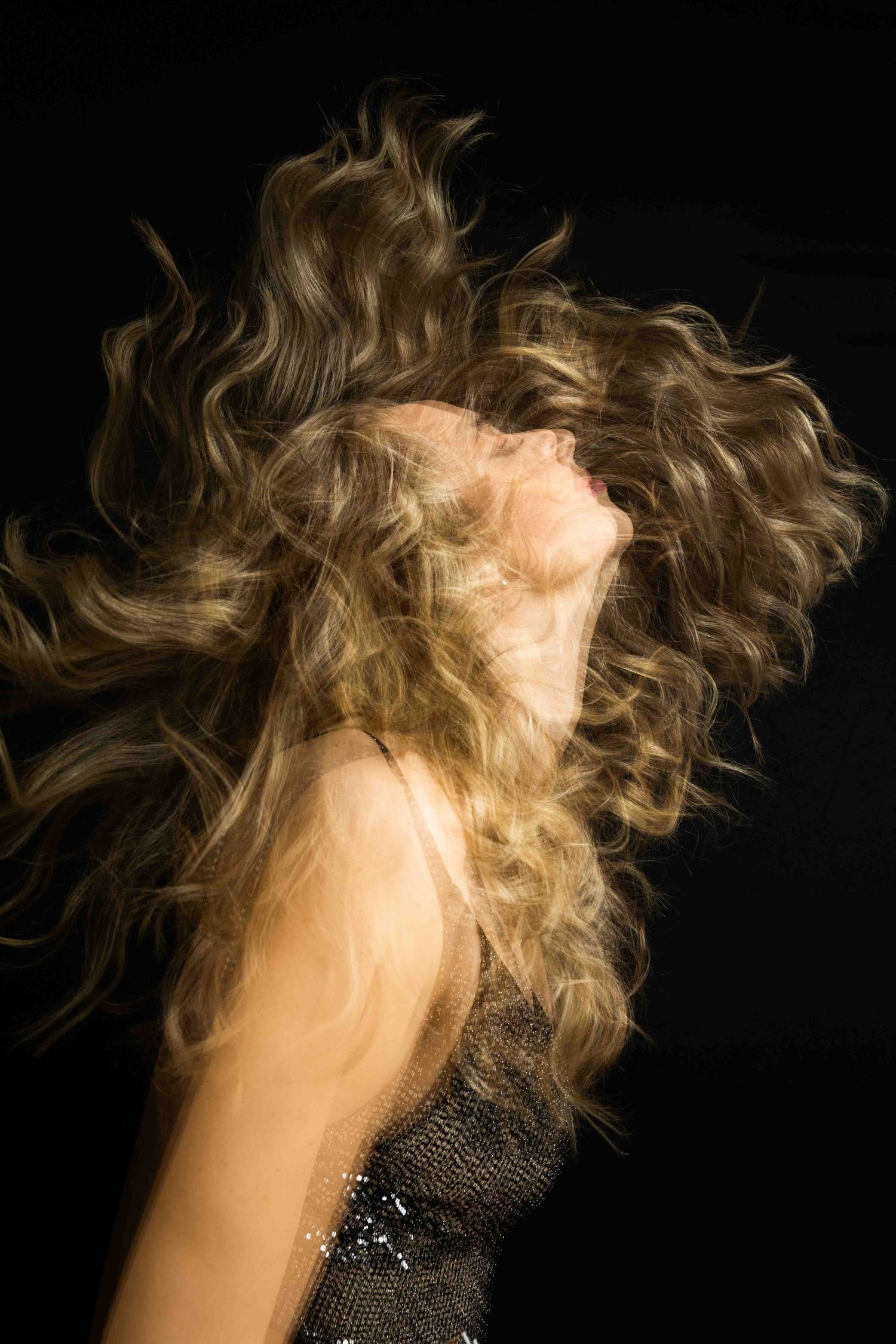 Fashion photo of blonde wavy hair in motion against dark background with sparkly dress.