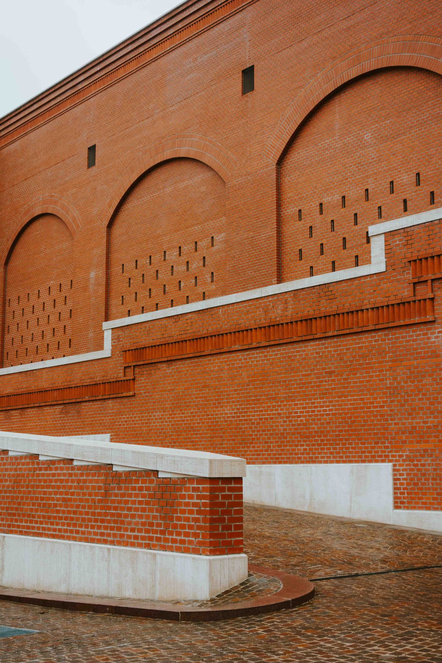 Modern architectural detail showing red brick wall with geometric arches and stepped design elements against concrete accents.