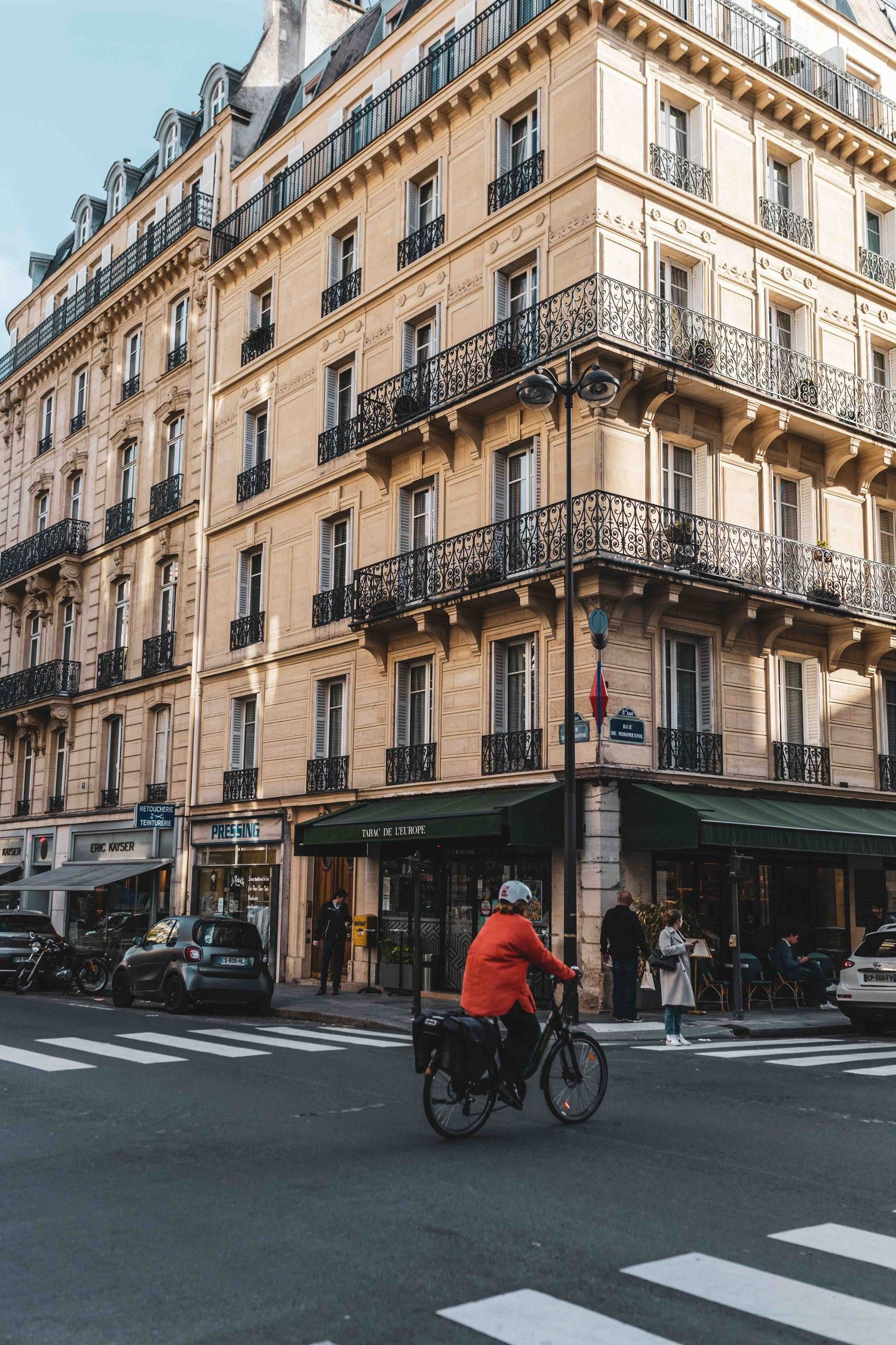 Elegant Parisian street corner showcasing classic Haussmann architecture with ornate balconies and a cyclist passing by.