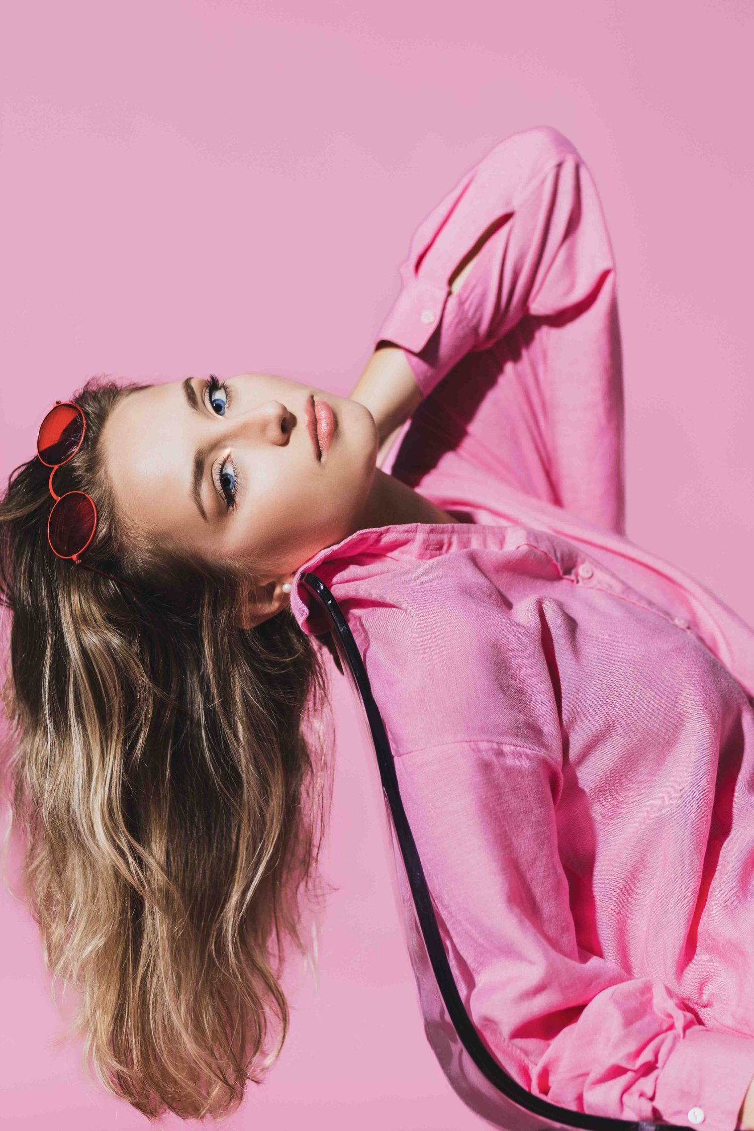 Fashion portrait with pink monochromatic styling and retro sunglasses against pink background.