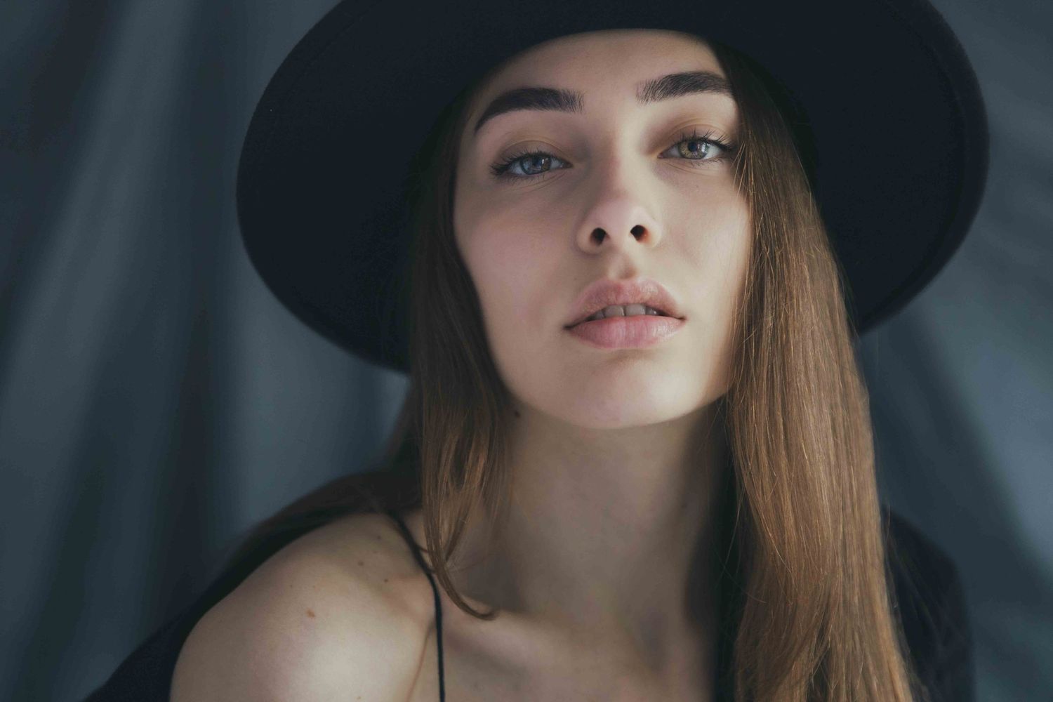 Fashion portrait of a person in a black wide brim hat with brown hair and dark background.
