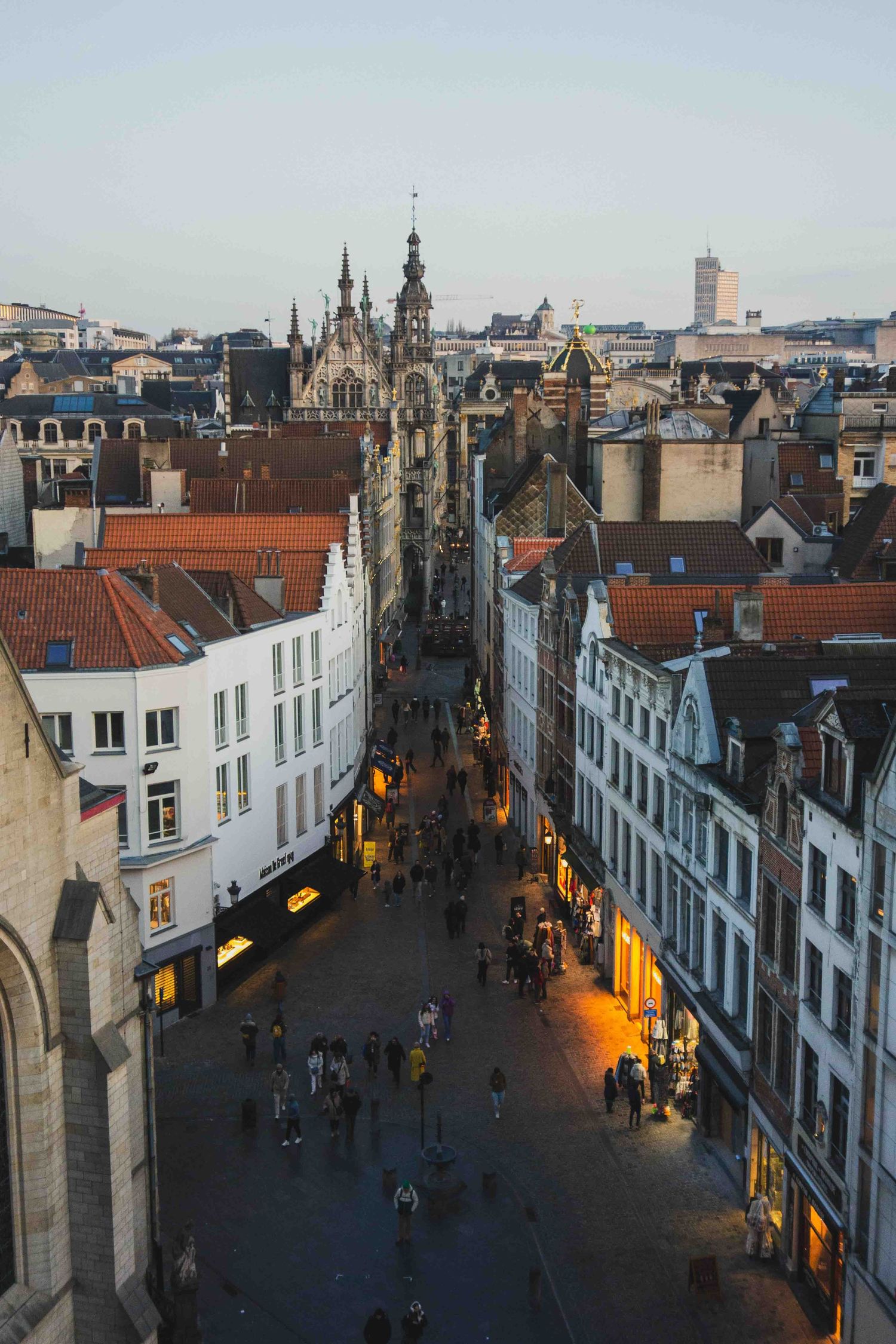 Aerial view of historic Brussels city street at dusk with Gothic architecture and warm glowing streetlights.