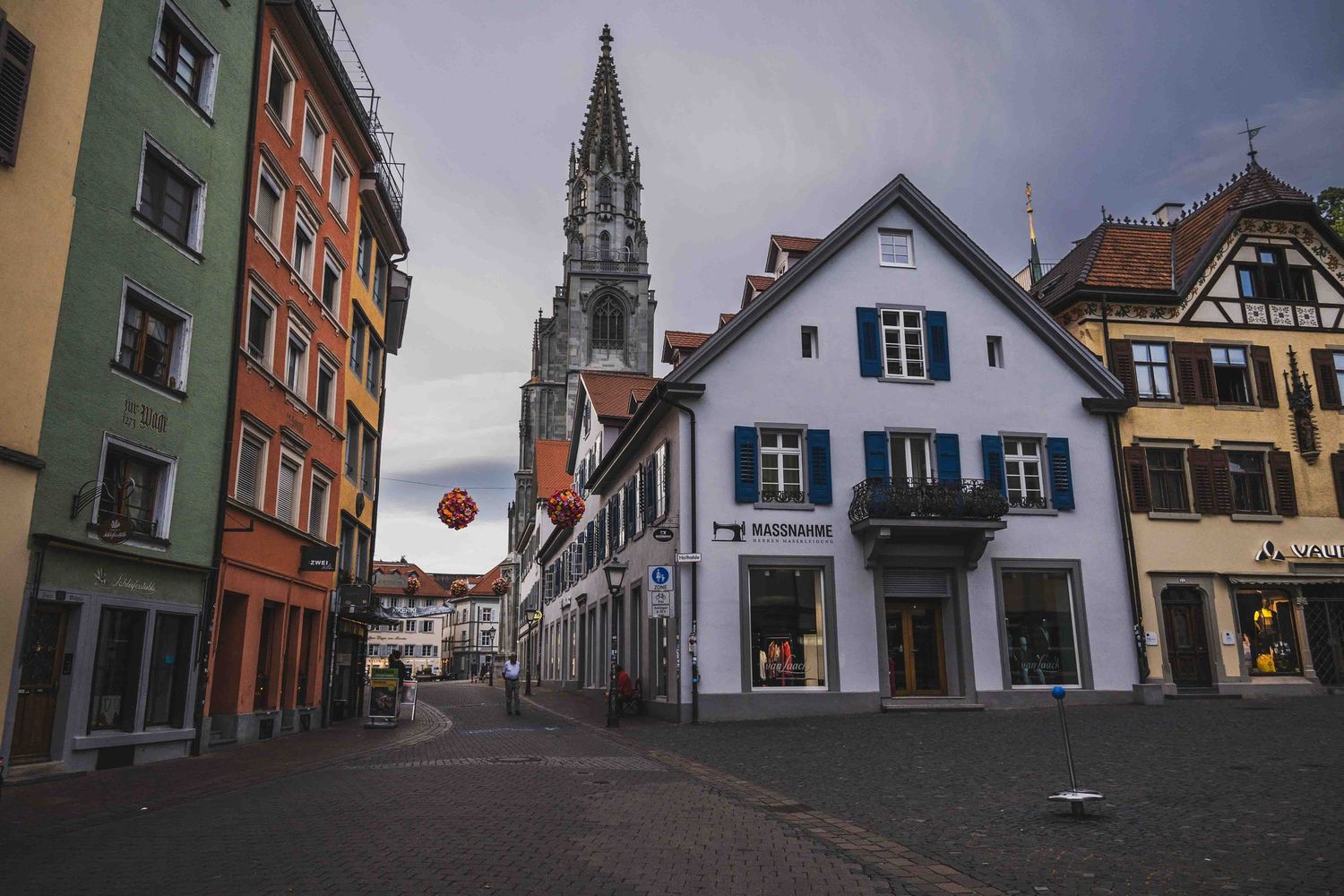 Historic European street with pastel buildings and Gothic church spire in Konstanz, Germany leads to charming town square.
