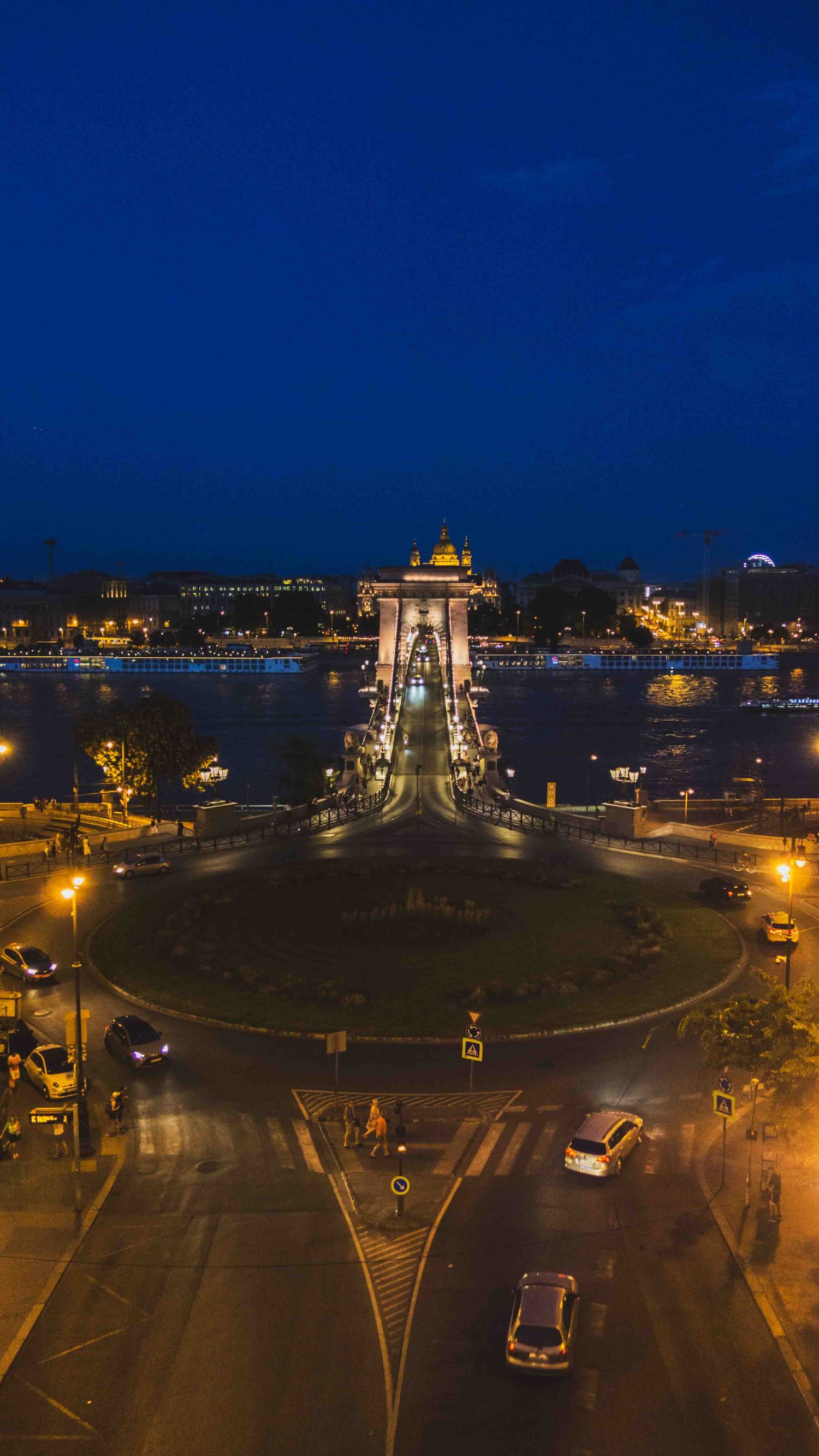 Panoramic nighttime series of illuminated city traffic circle and streets with cars and buildings in blue hour lighting.