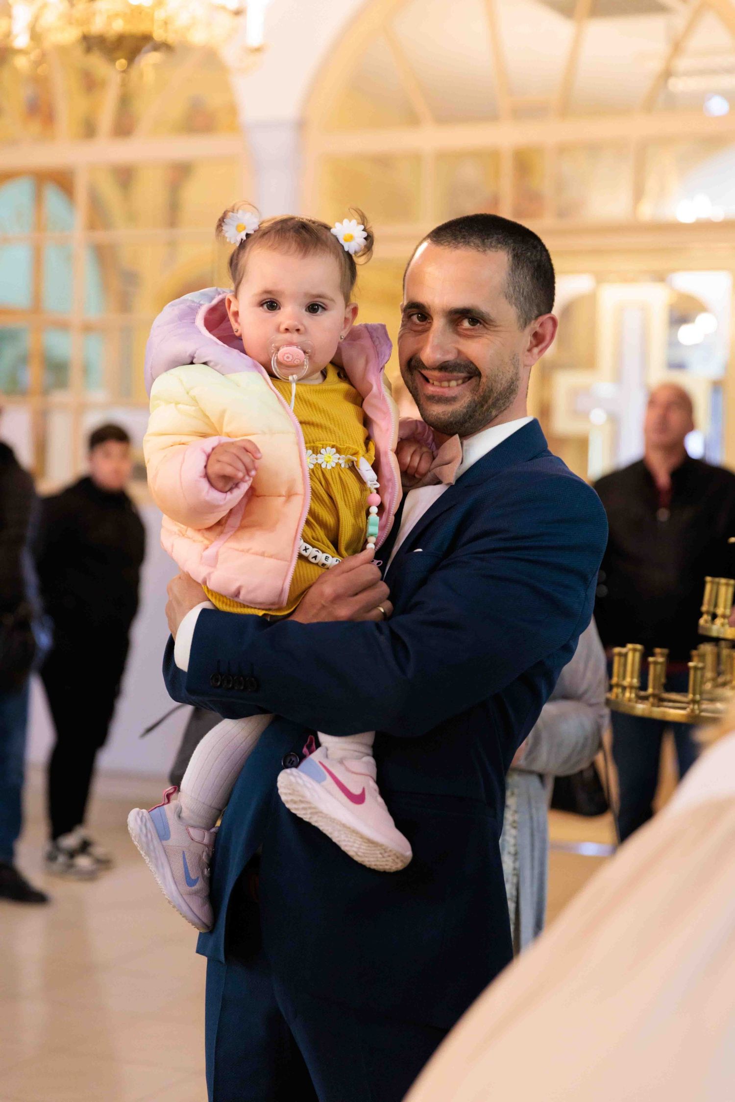 A father in a navy suit dances with a small child wearing pink at an elegant indoor reception venue.