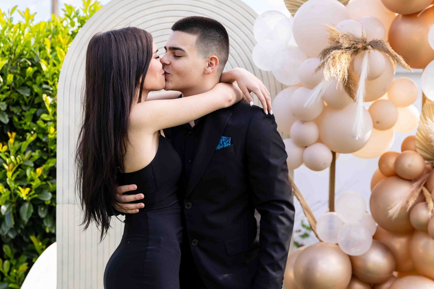 Couple shares a tender moment against backdrop of rose gold balloon decorations at an elegant celebration.