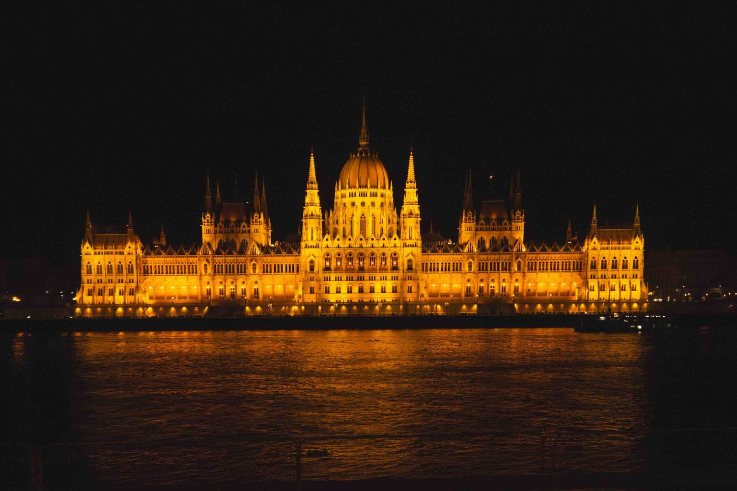 The illuminated Hungarian Parliament Building reflects golden light on the Danube River at night in Budapest.