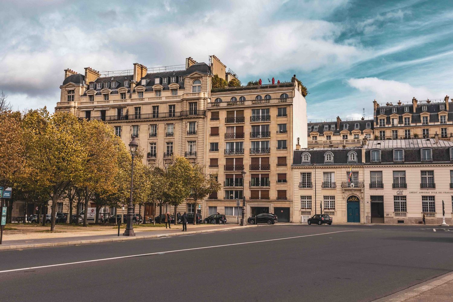 Panoramic view of classic Parisian apartment buildings and historic architecture along a tree-lined street in Paris.
