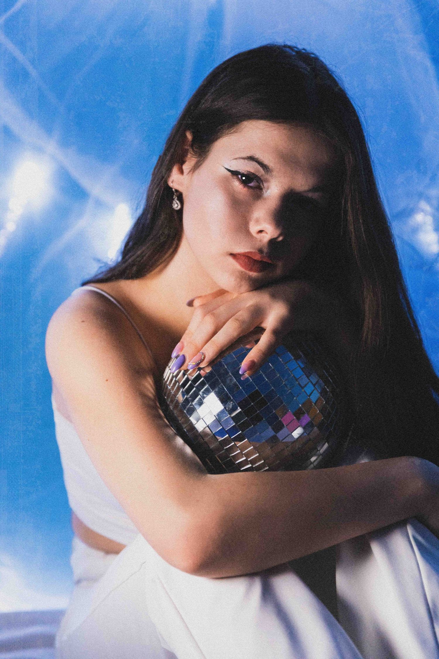 Artistic portrait holding disco ball against blue sky backdrop in dreamy aesthetic style.