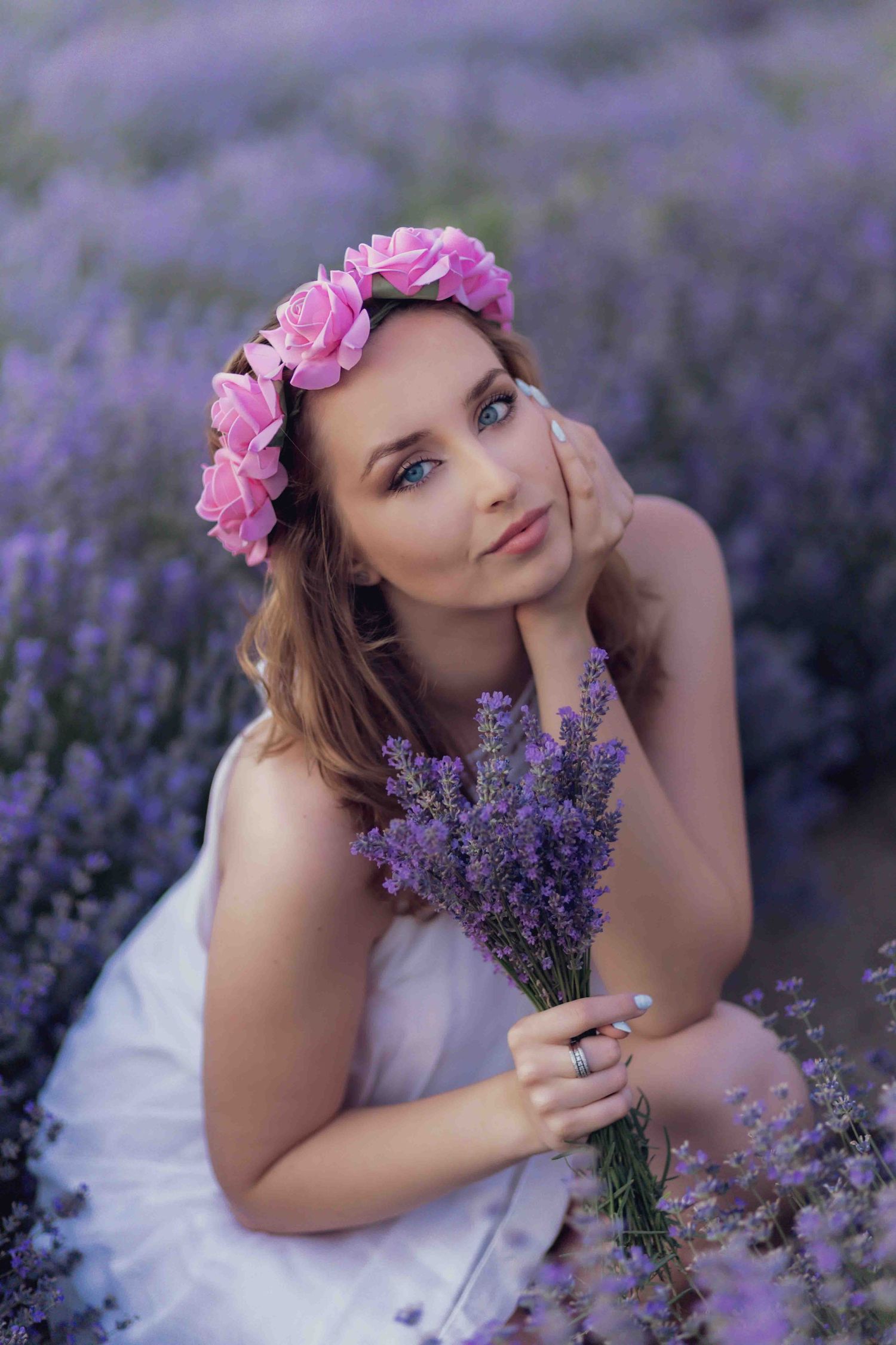 Someone wearing a pink flower crown poses gracefully among blooming purple lavender flowers in a dreamy summer photo series.
