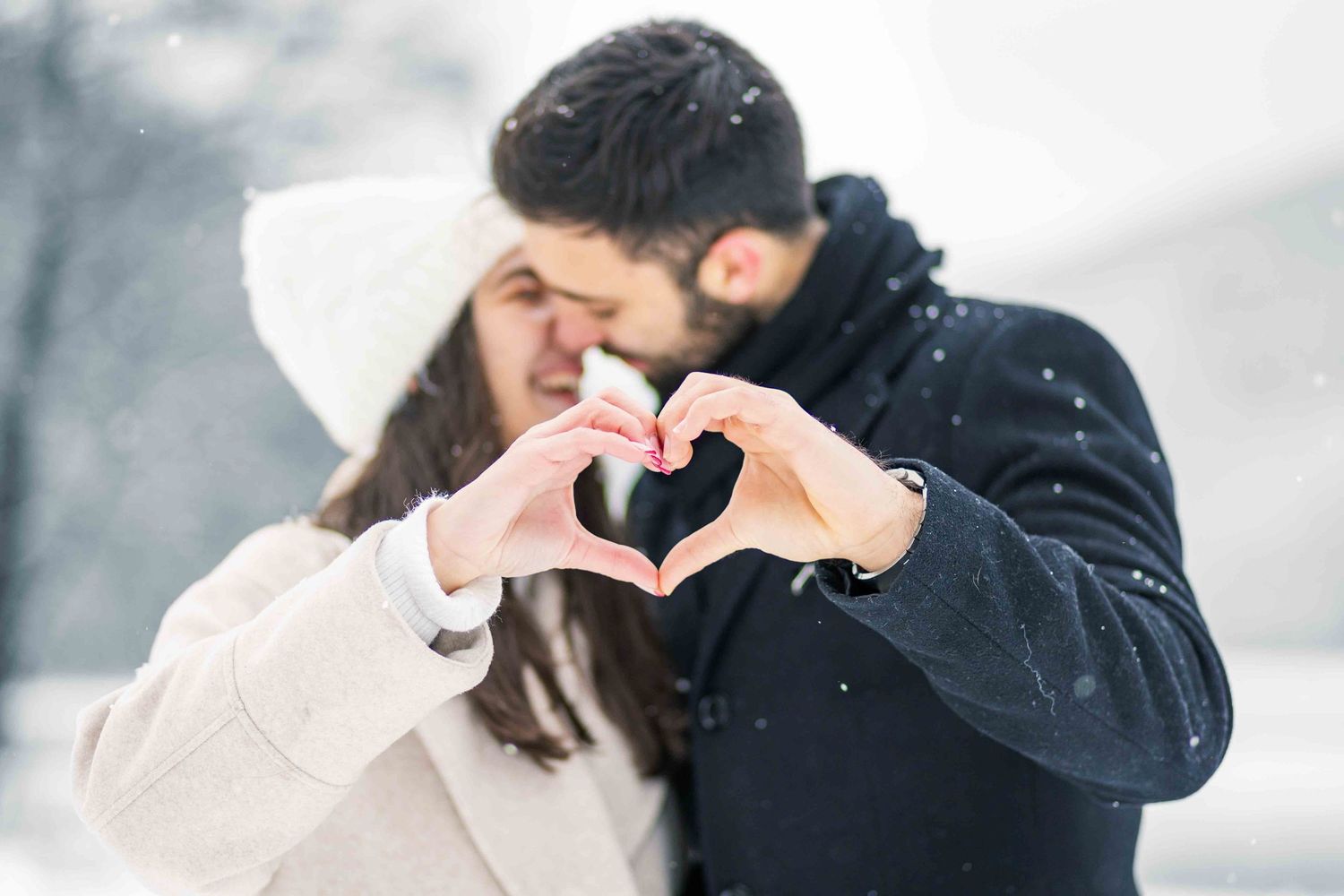 A couple embraces and kisses during a romantic winter snow session, wearing cozy dark and light colored coats.