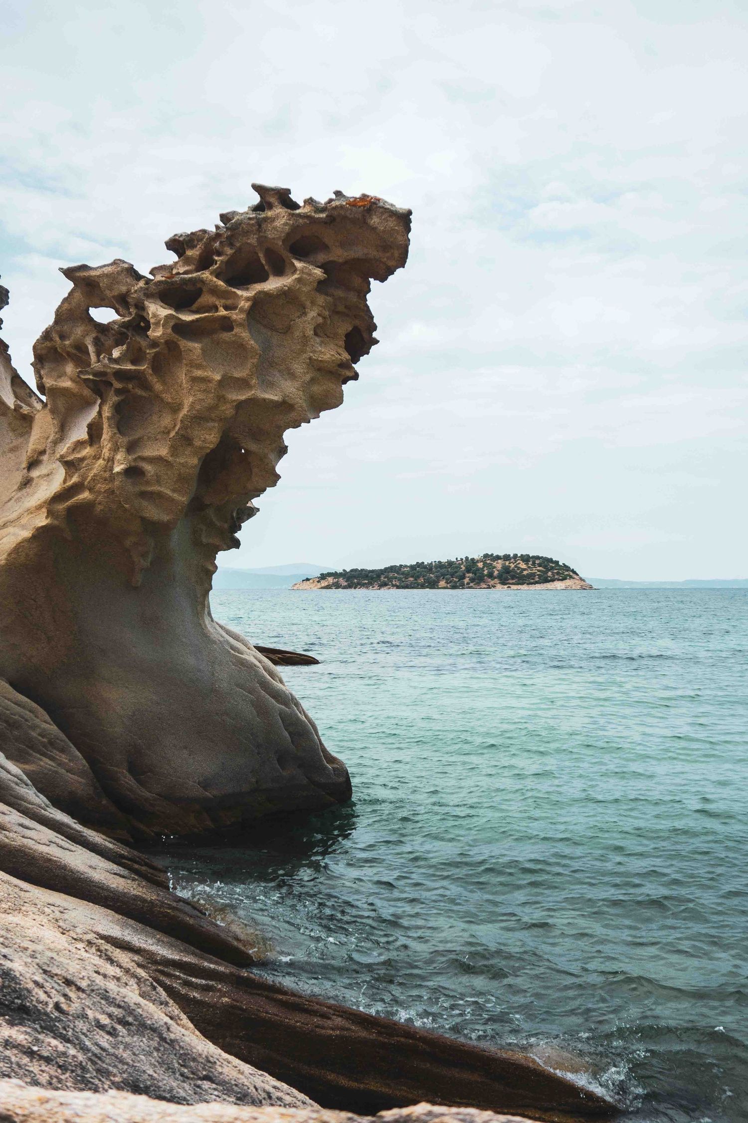 Weathered coastal rock formations and caves along turquoise ocean waters with a small island visible in the distance.