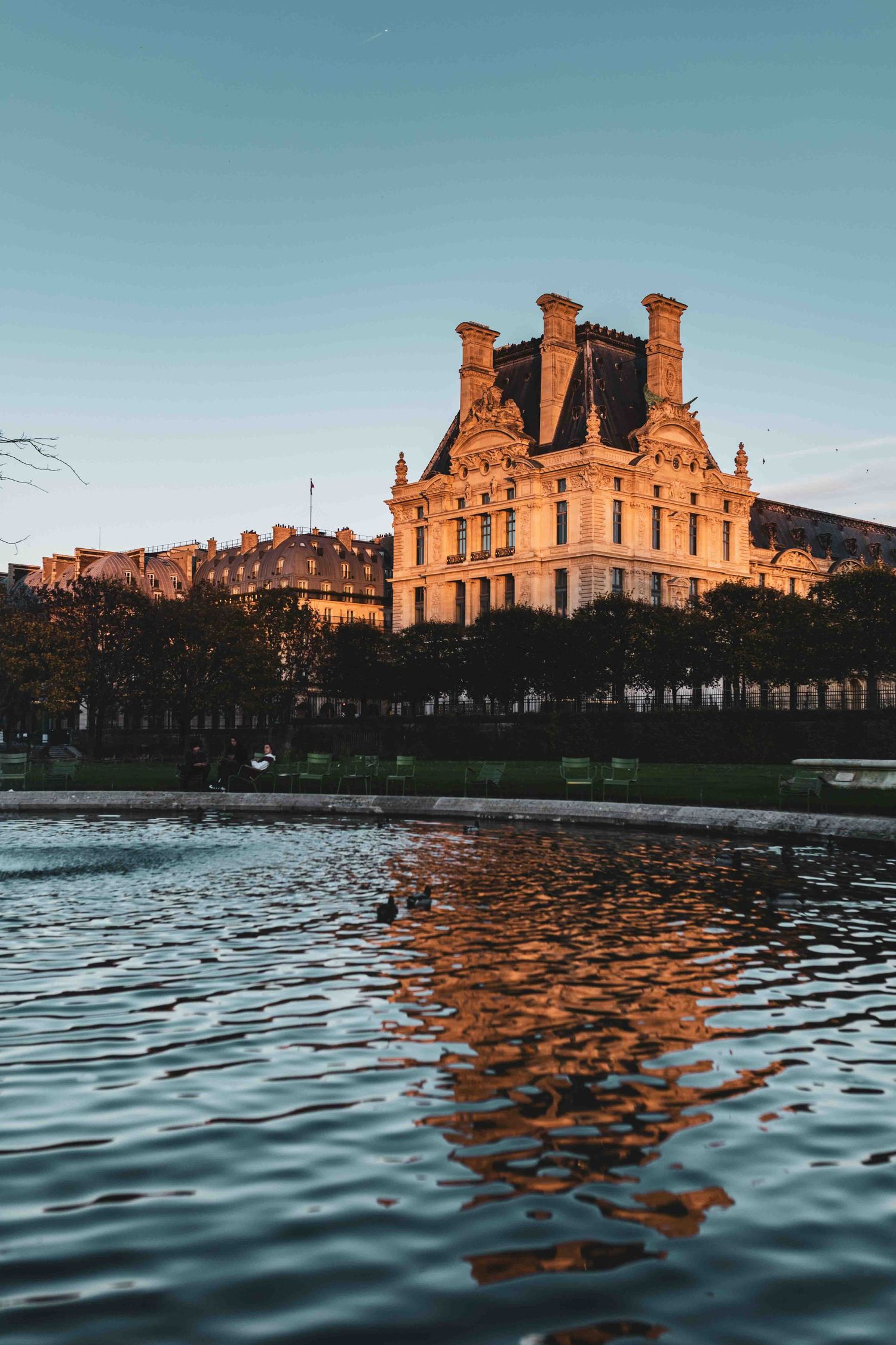 Reflection of the Louvre Palace in water at sunset with golden light illuminating its ornate Renaissance architecture.