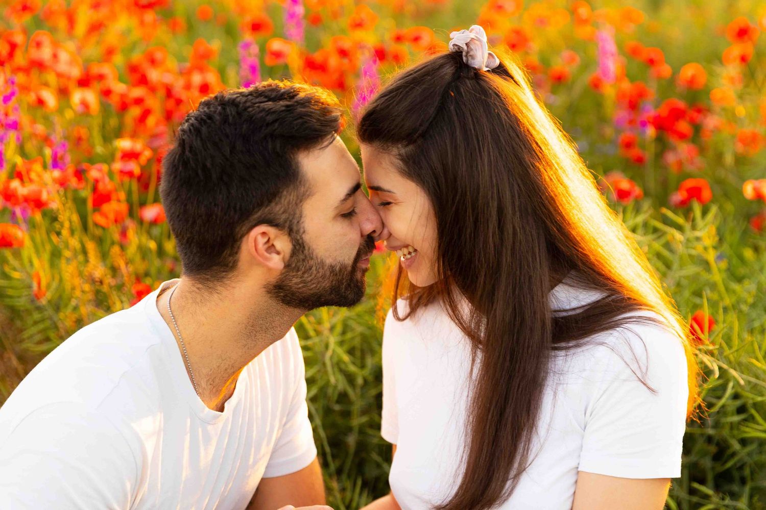 A romantic couple shares an intimate moment in a vibrant field of red and orange wildflowers at sunset.
