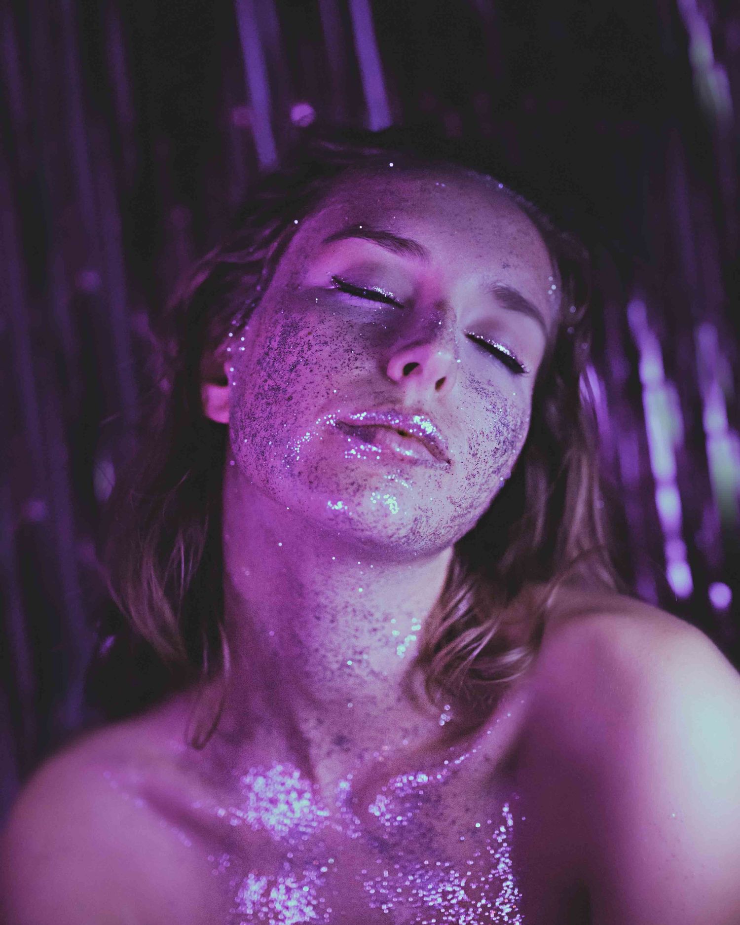 Artistic portrait with purple glitter and dramatic lighting creating a magical effect.