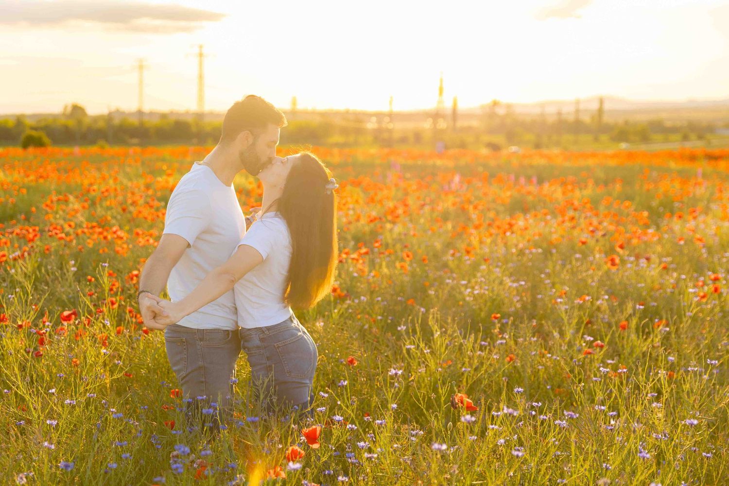 A couple embraces in a golden field of wildflowers at sunset, creating a romantic silhouette against the warm light.