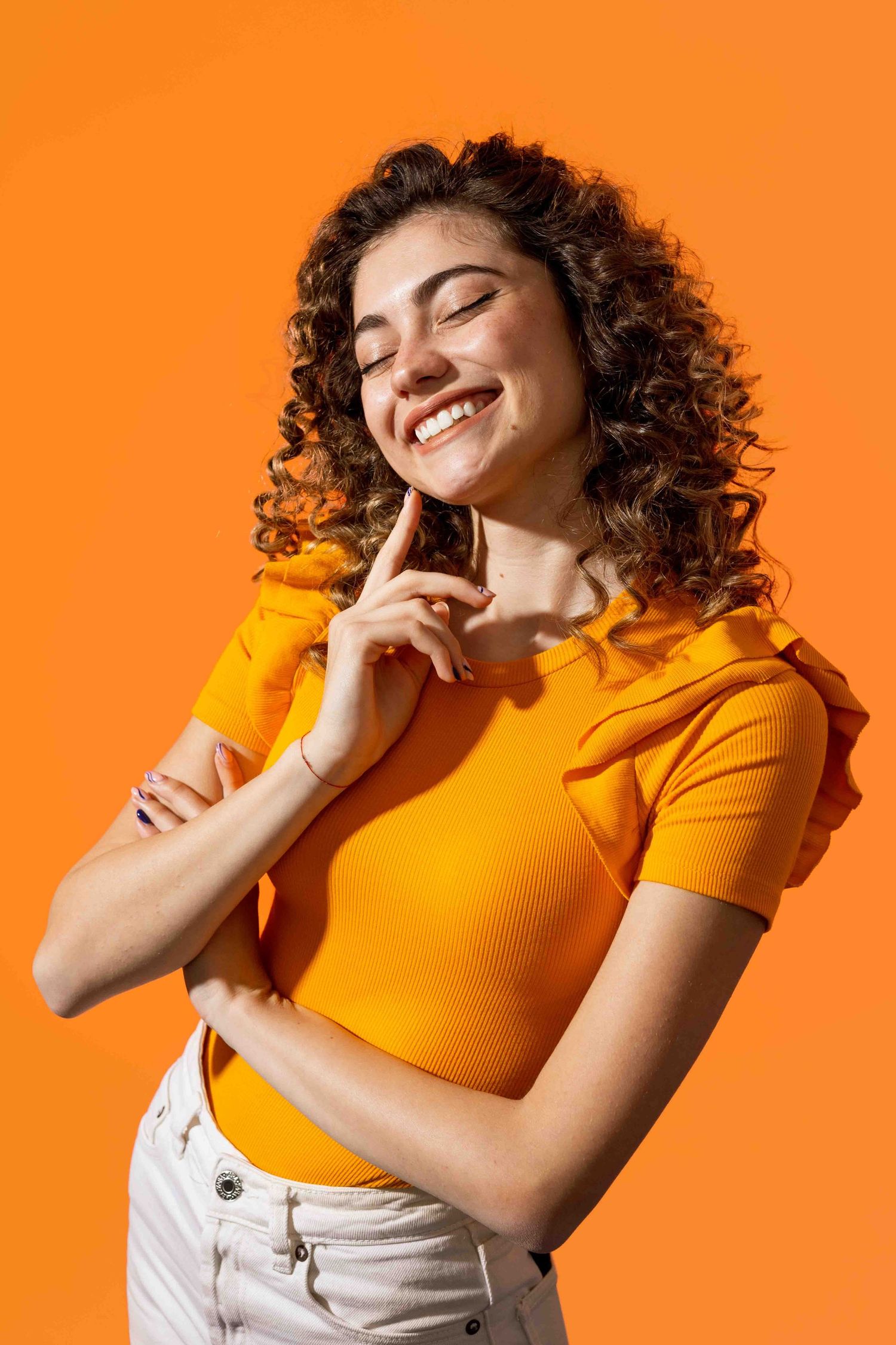 Person in orange shirt smiling with curly hair against vibrant orange background.