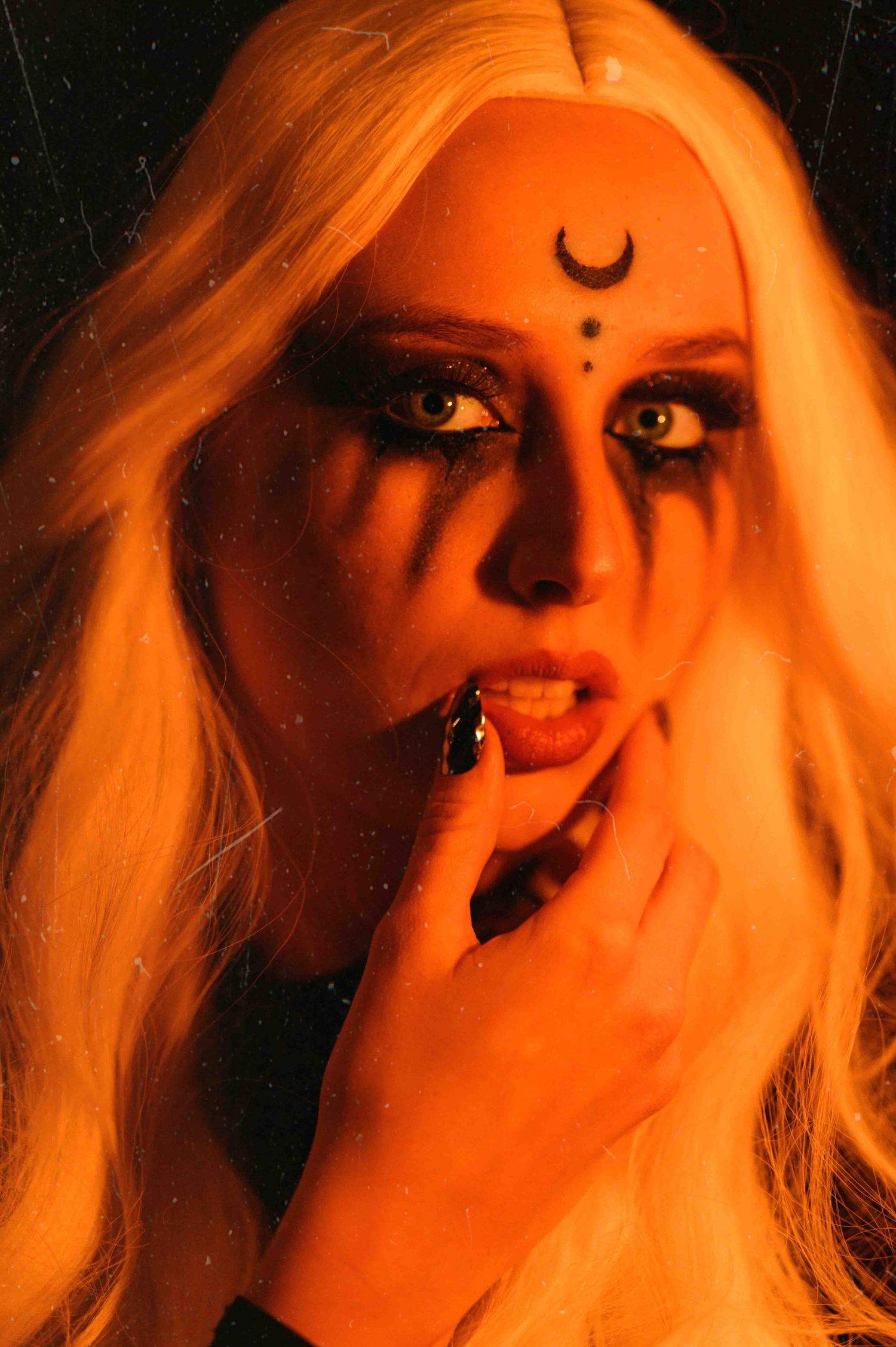 Creative portrait with gothic moon makeup and dramatic orange lighting creating a mystical mood.