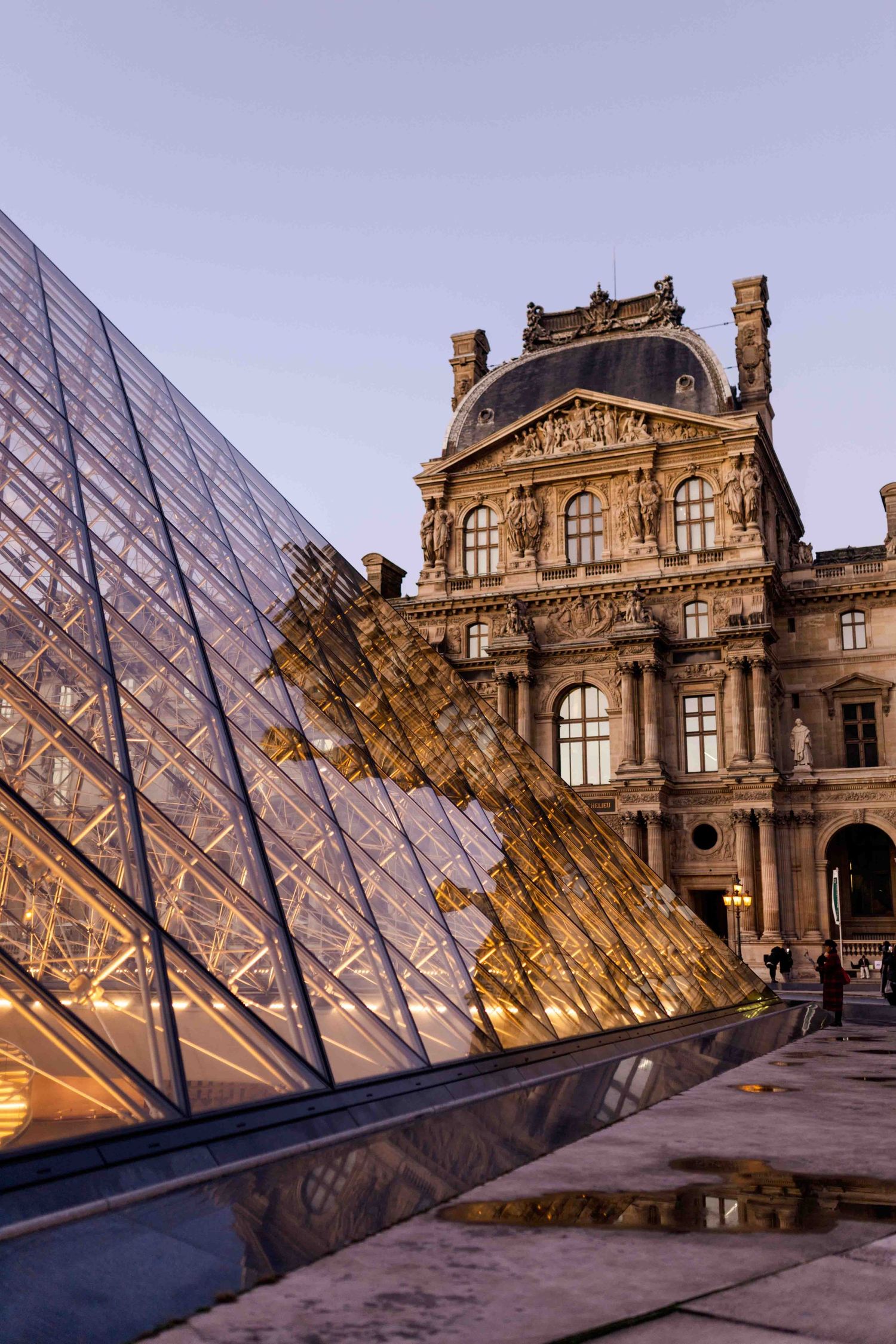 The Louvre Museum's glass pyramid entrance reflects golden light at dusk against the historic Parisian palace architecture.