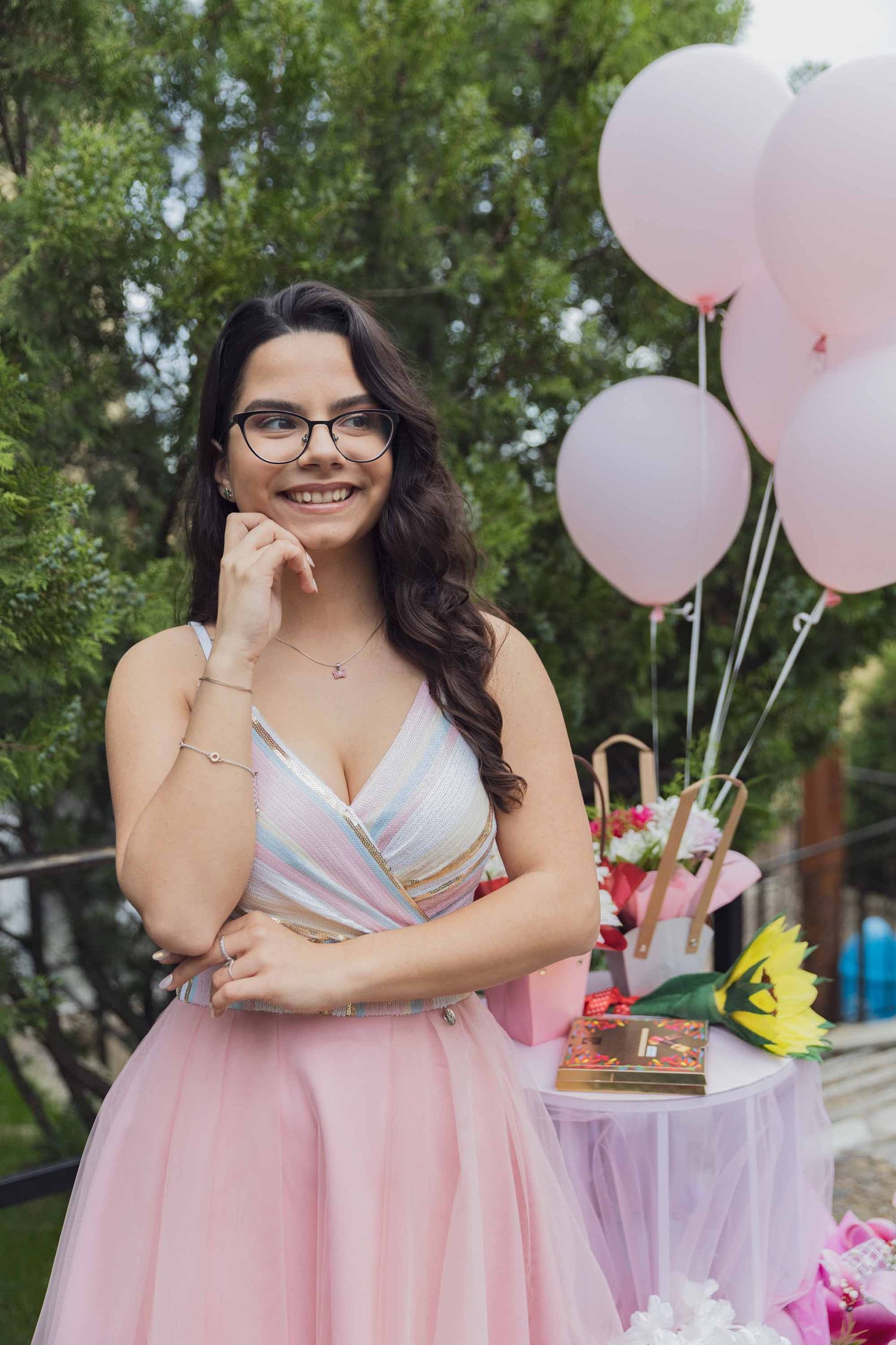 Pretty pastel party setup with pink tulle dress, pale balloons and decorated table in garden setting.