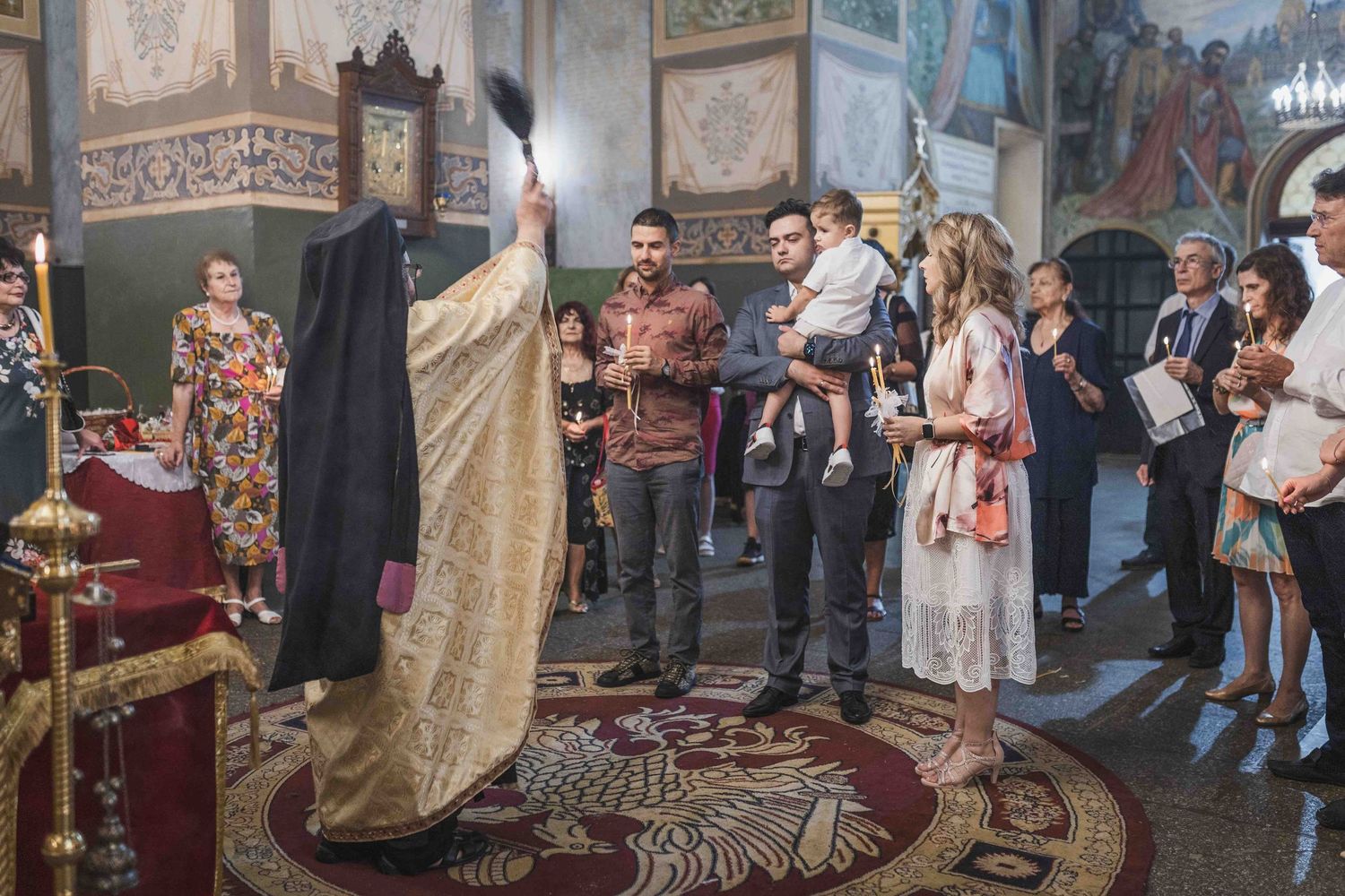 Orthodox priest performs religious ceremony in ornate church interior while congregation watches and participates.