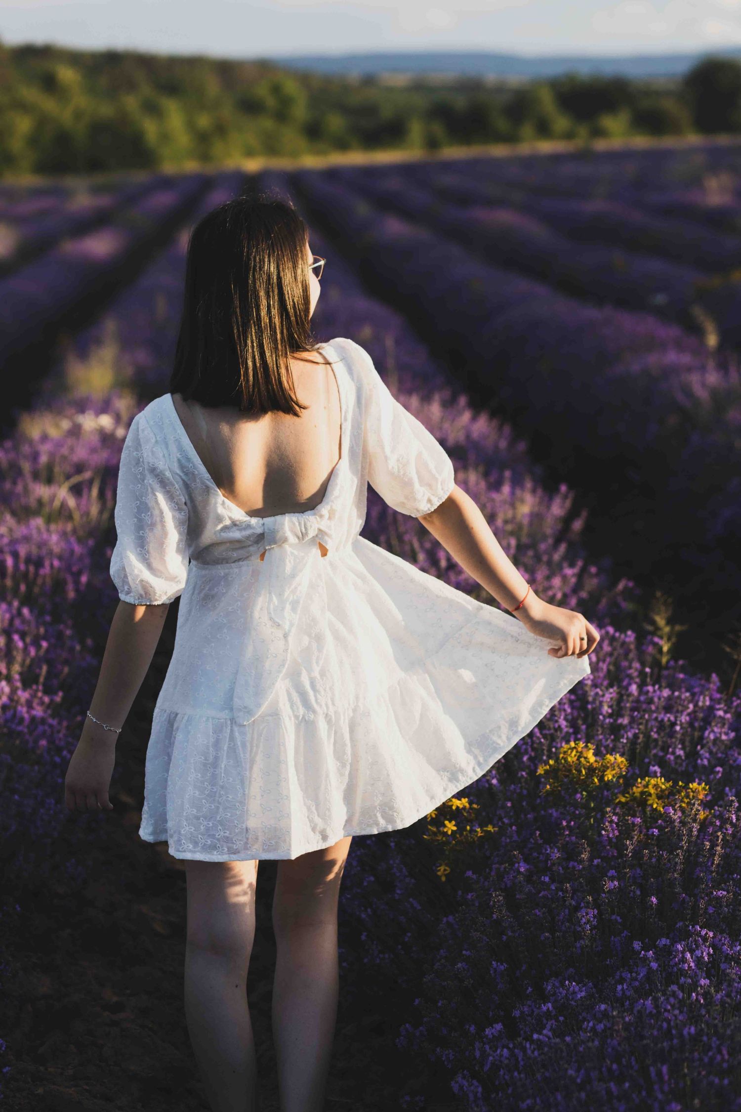 A white dress flows gracefully through rows of blooming purple lavender fields at sunset creating a dreamy scene.